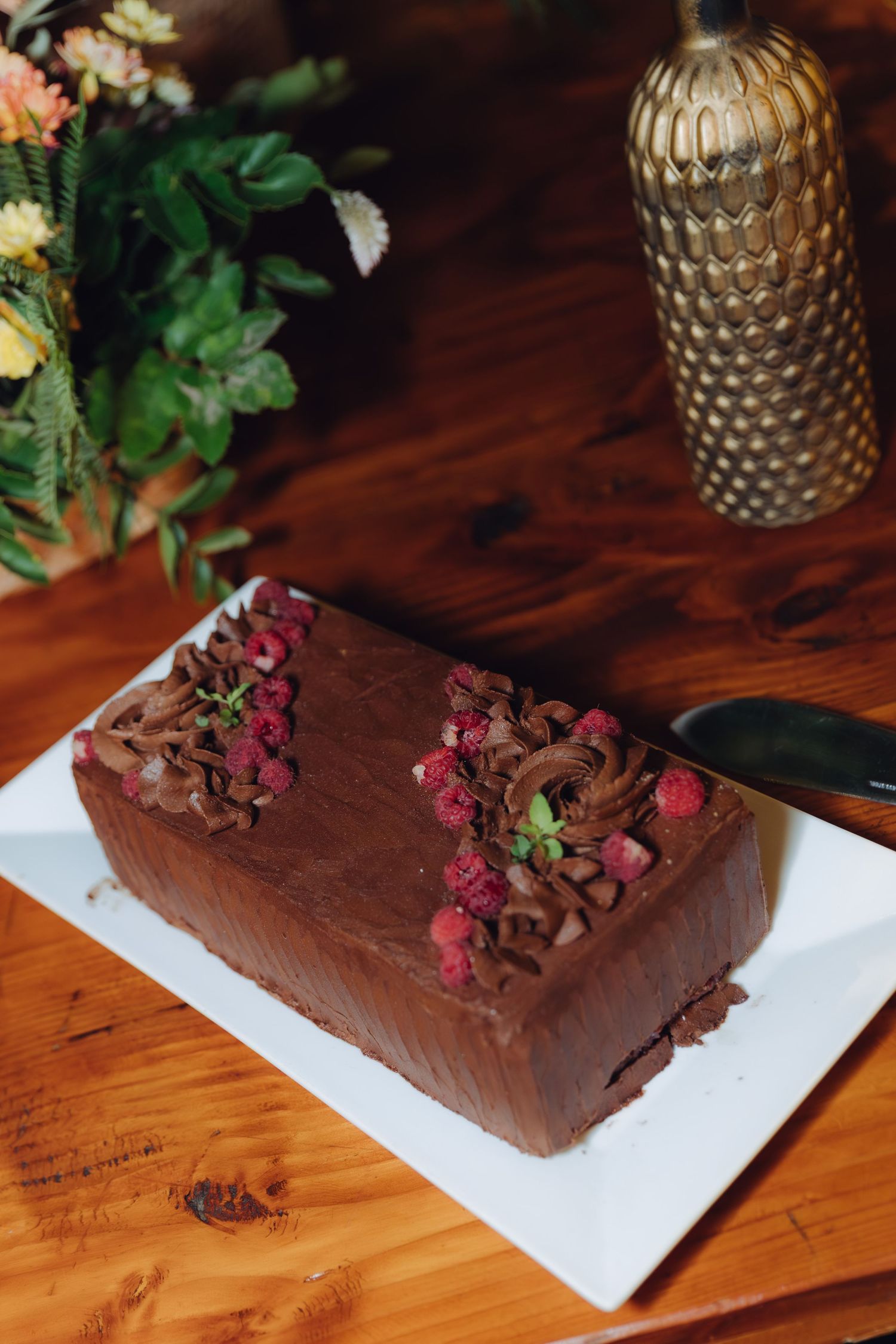 Rectangular chocolate cake with raspberry and mint garnish on a white plate at a wedding reception.