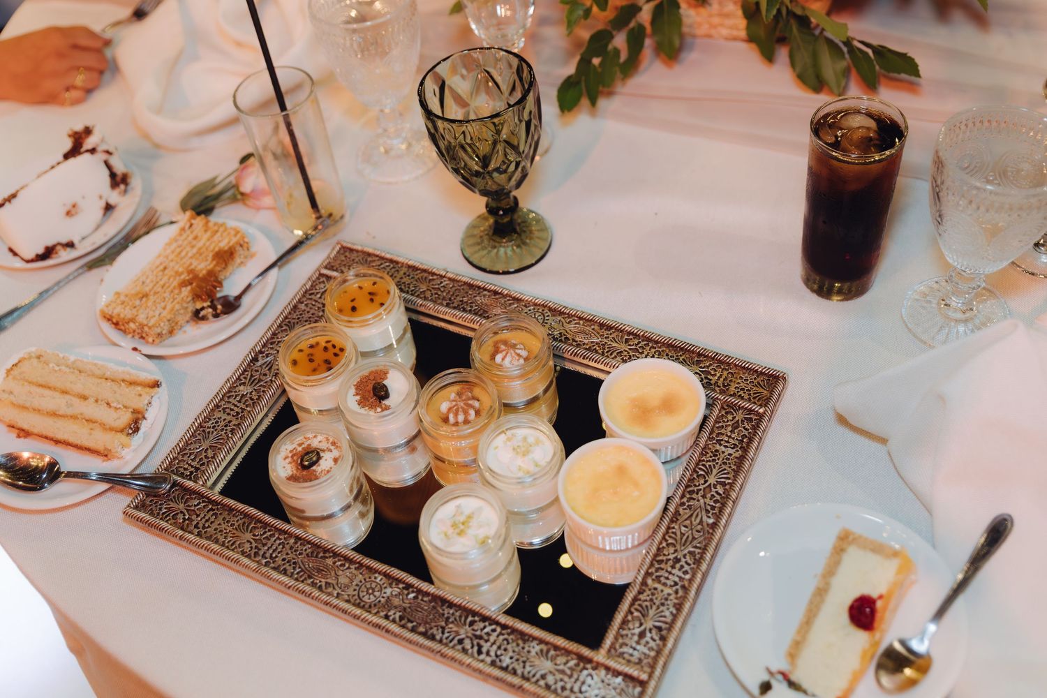 Wedding dessert display with assorted creme brulee and mousse cups arranged on an ornate mirrored tray.