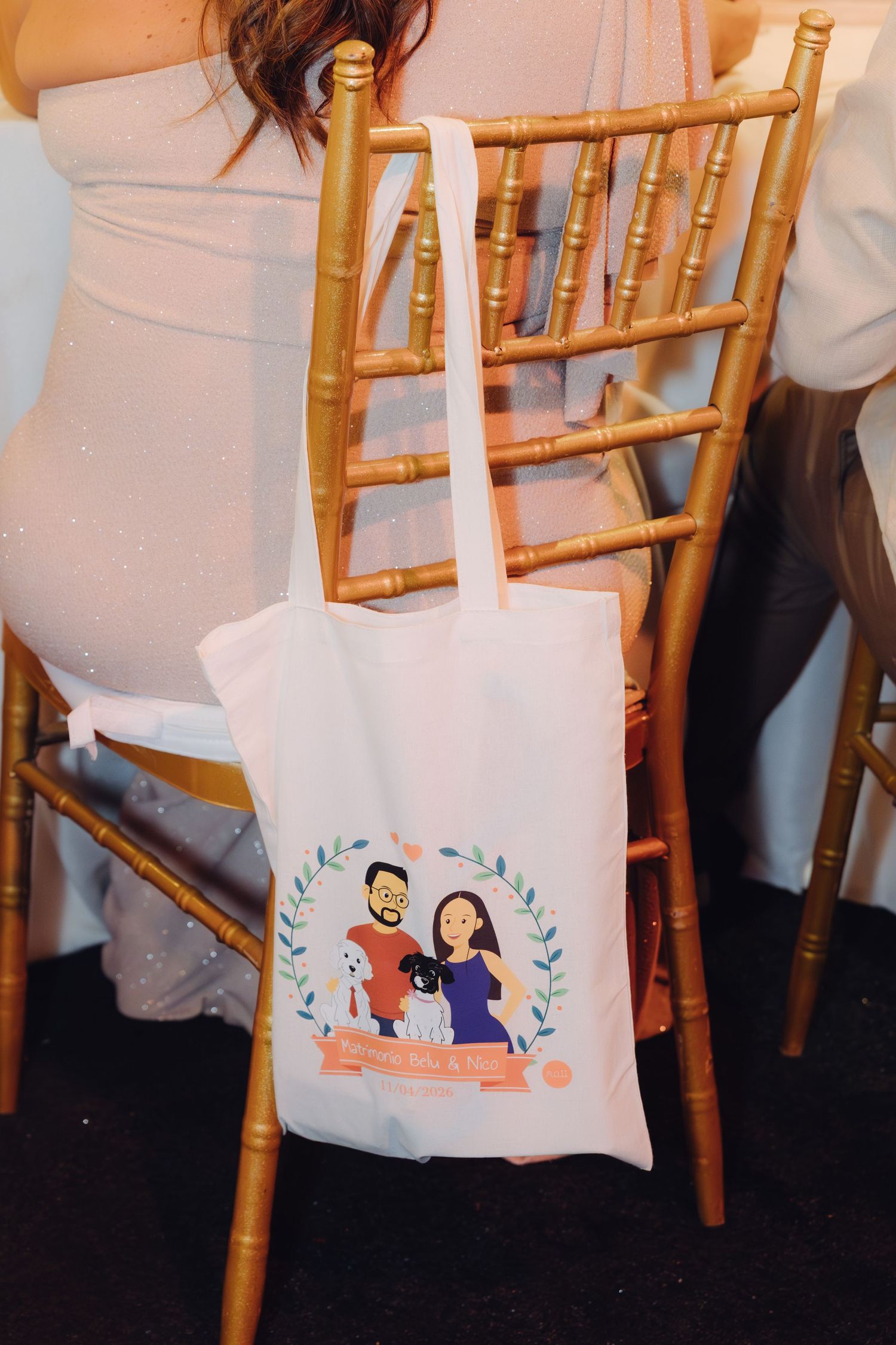 Custom illustrated wedding tote bag featuring couple and pets hanging on a gold chiavari chair.