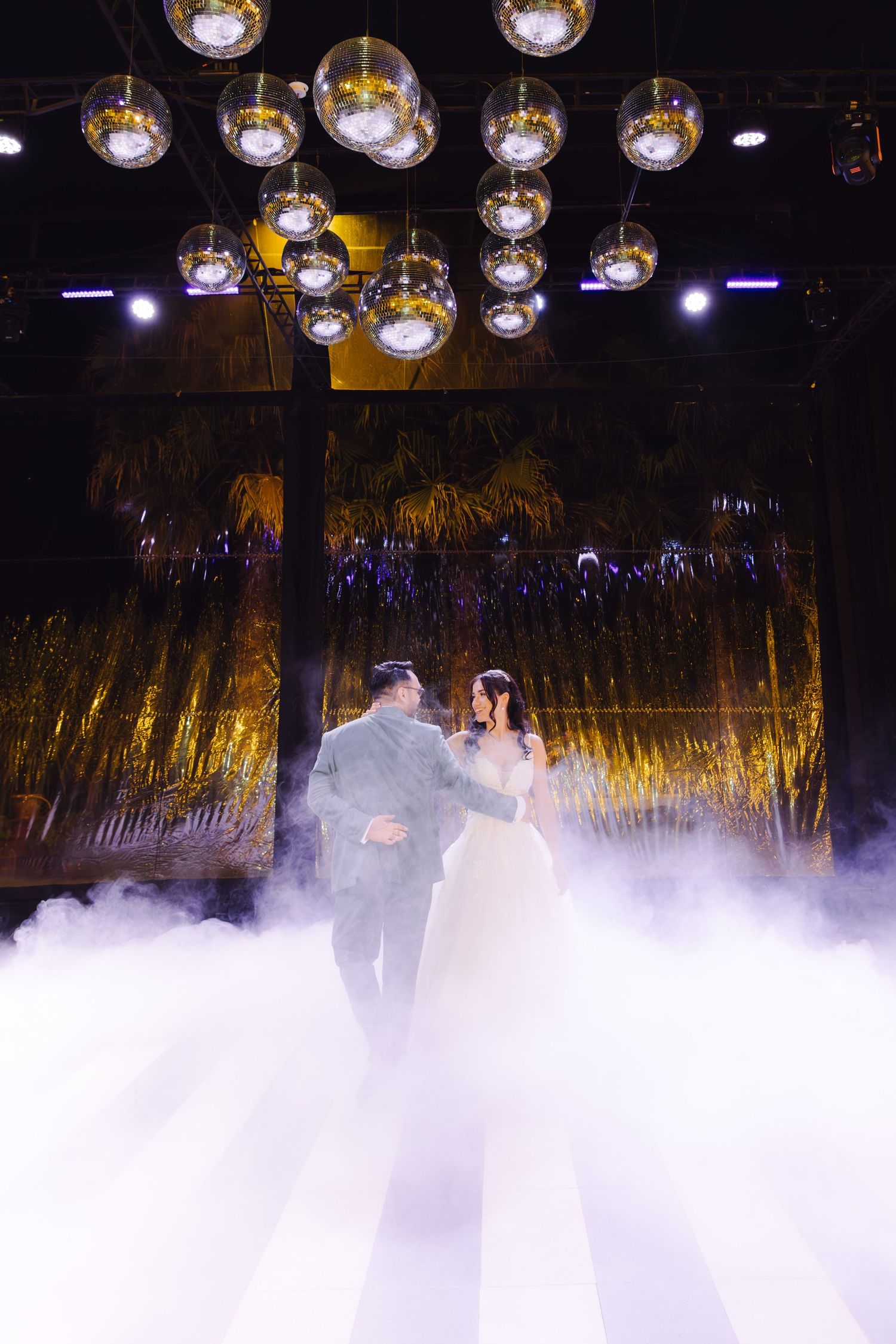 Bride and groom share first dance on fog-covered dance floor under glowing globe lights at elegant wedding reception.