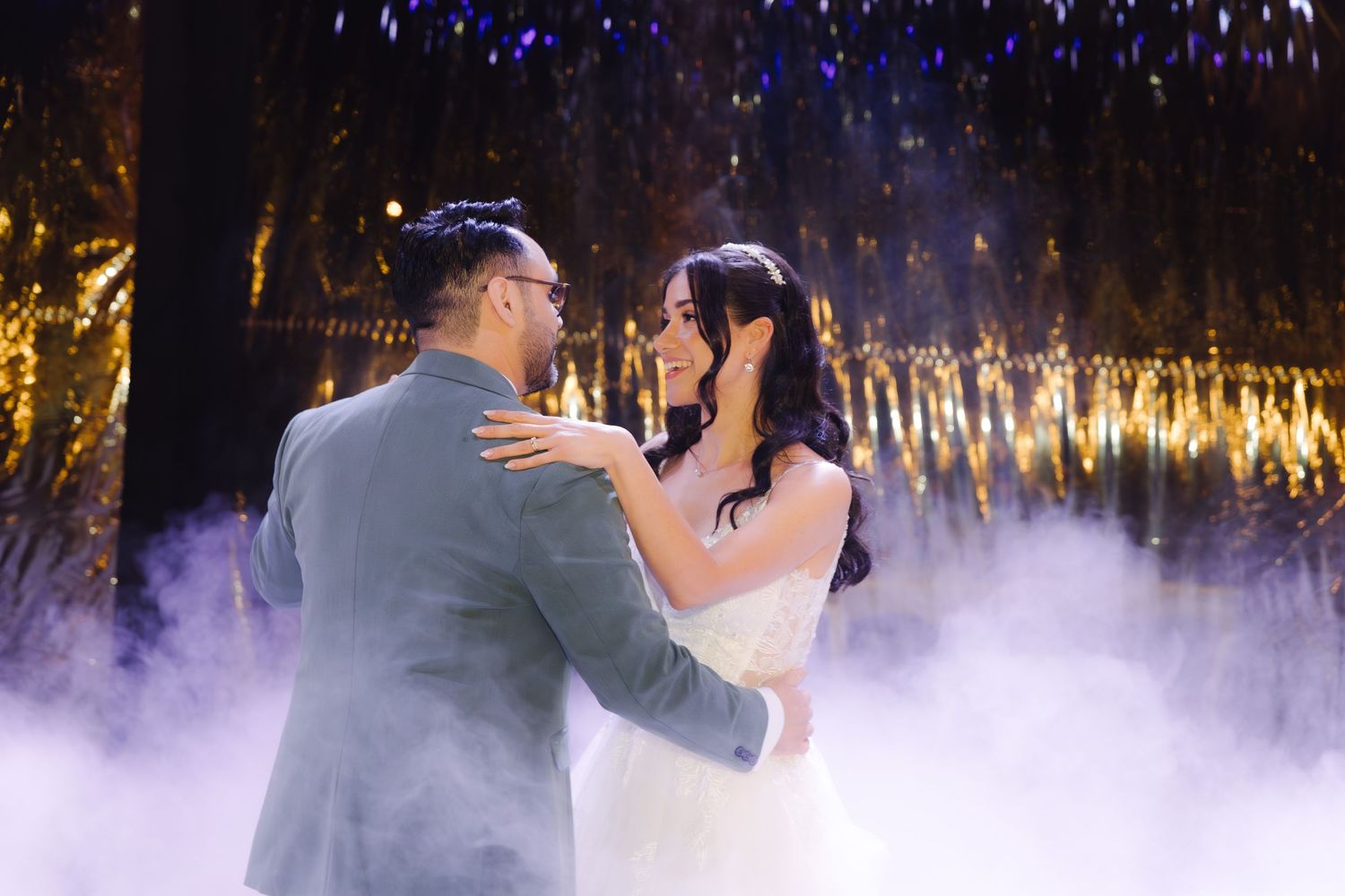 Newlyweds share an intimate first dance moment surrounded by dreamy fog and golden bokeh lights at wedding.