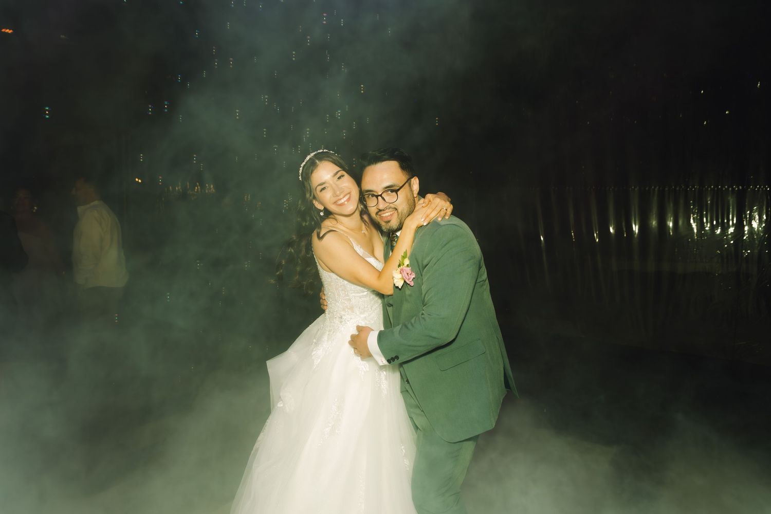 Happy bride and groom embrace on foggy dance floor in candid film-style wedding reception photograph.