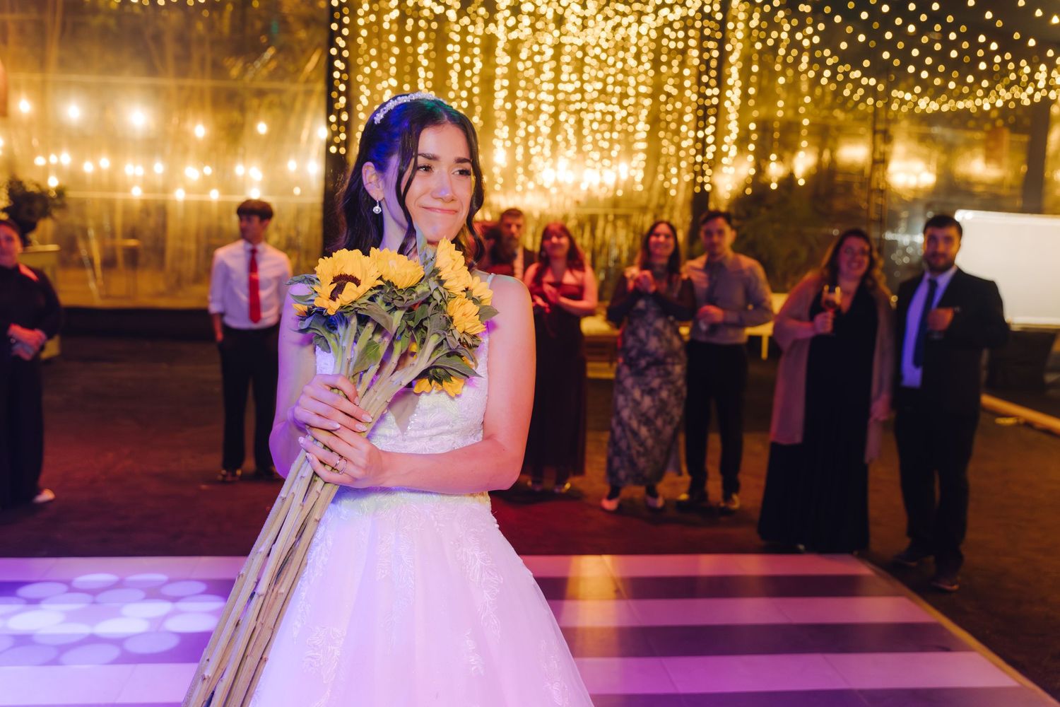 Bride holding sunflower bouquet on dance floor preparing for bouquet toss at wedding reception.