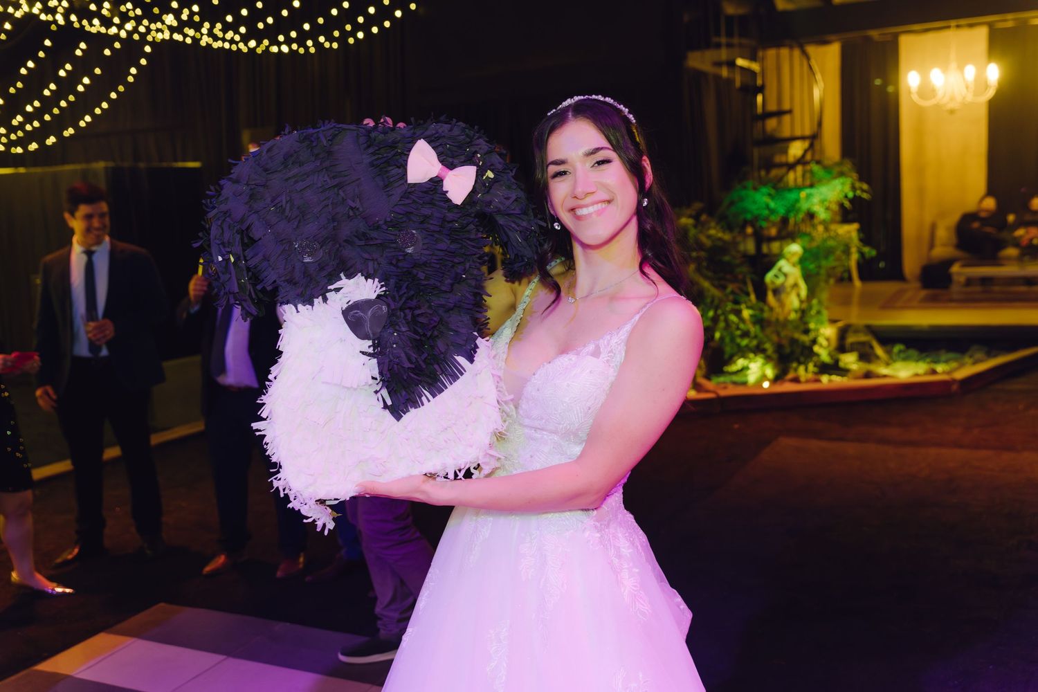 Young woman in pink ball gown holding black and white fluffy pinata at elegant party venue.