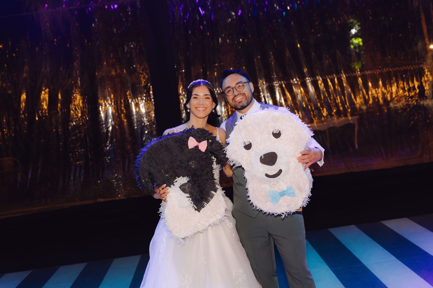 Bride and groom posing with black and white dog-shaped pinatas on striped wedding dance floor.