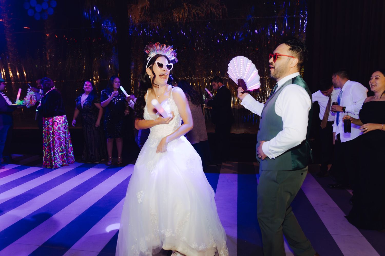 Bride wearing sugar skull mask and groom with fan dancing at festive wedding reception.