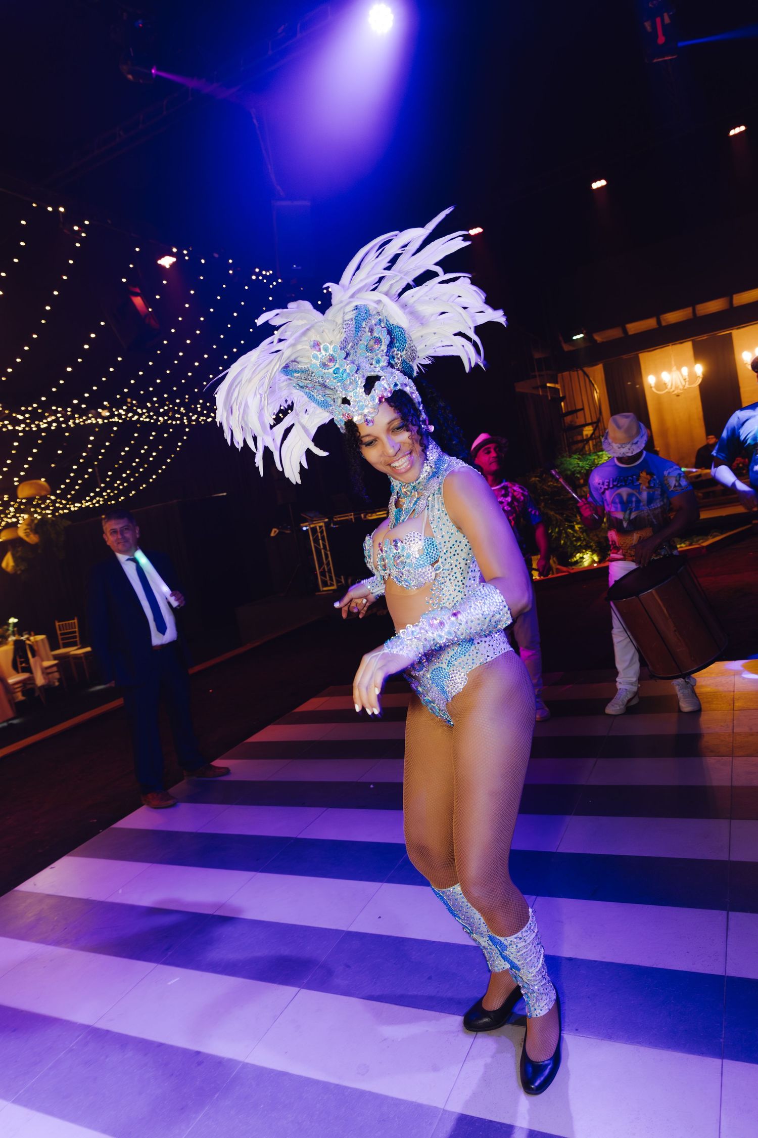 Samba dancer in sparkling white feathered costume performing on striped dance floor at wedding.