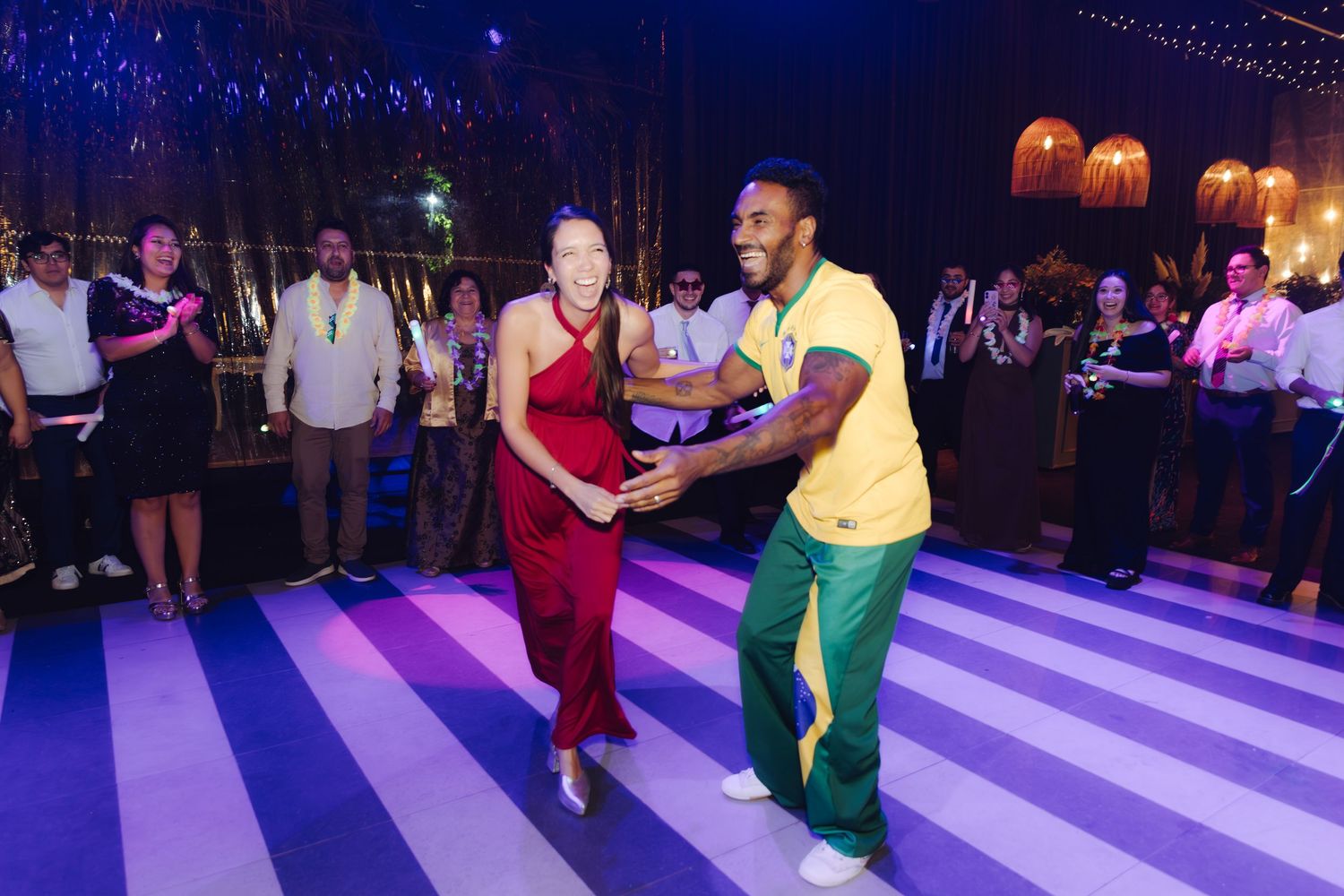 Couple in red dress and yellow jersey dancing energetically on a striped dance floor at a celebration.