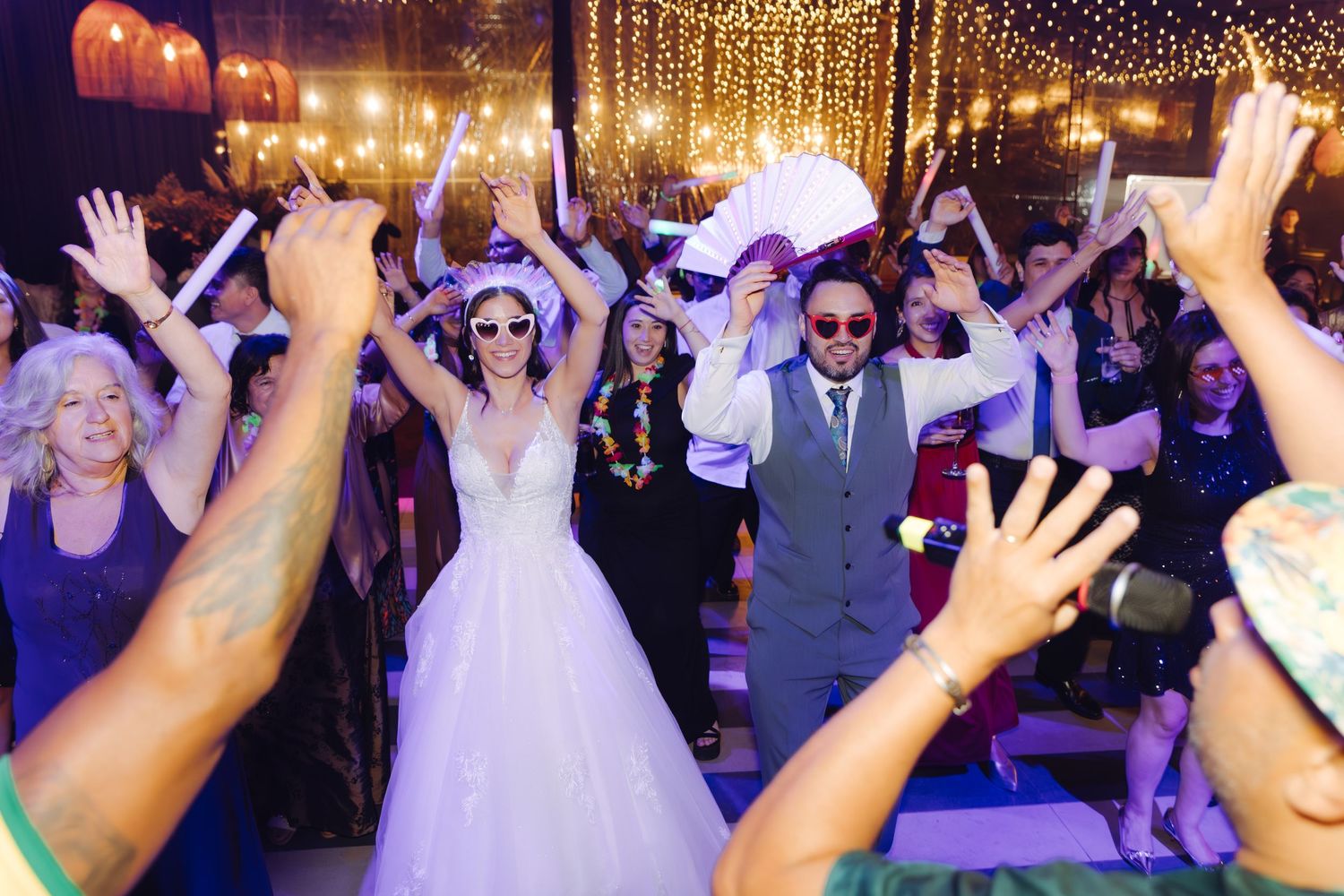 Newlyweds celebrate on the dance floor surrounded by cheering guests at a festive wedding reception.
