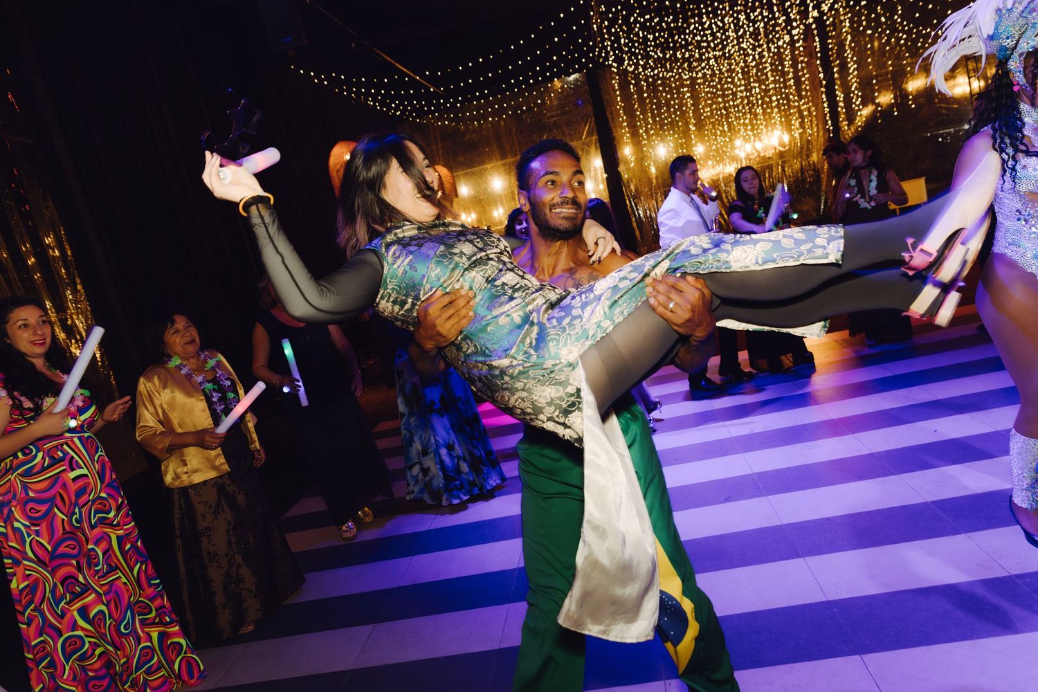 Performer lifts a guest dramatically on a striped wedding reception dance floor under string lights.