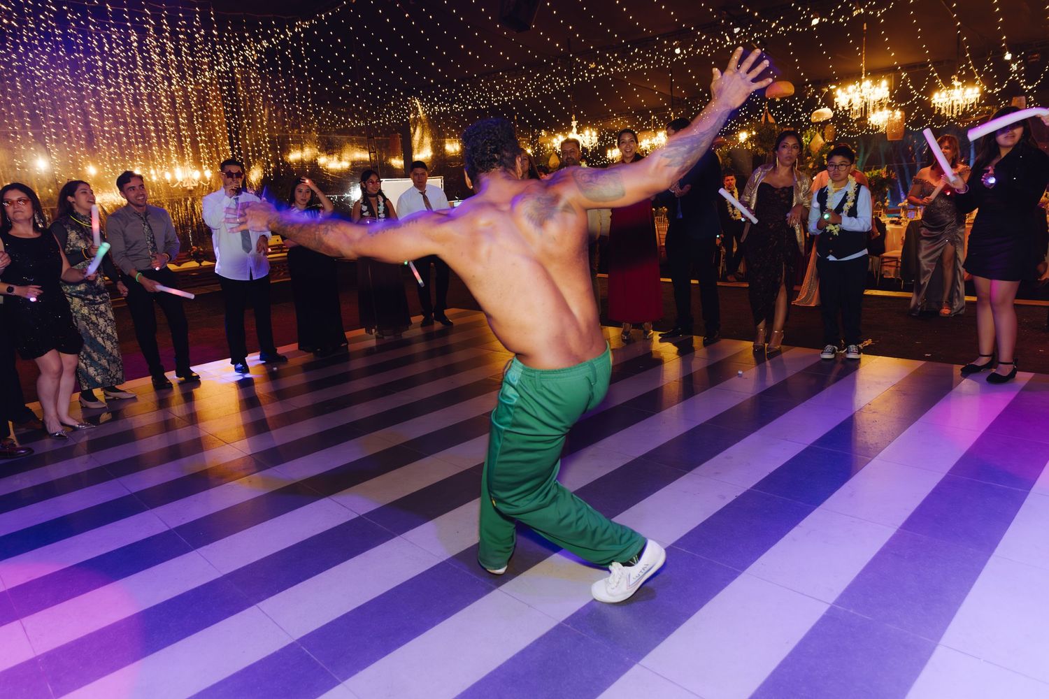 Shirtless acrobatic dancer performs a dramatic pose on a striped dance floor at a wedding.
