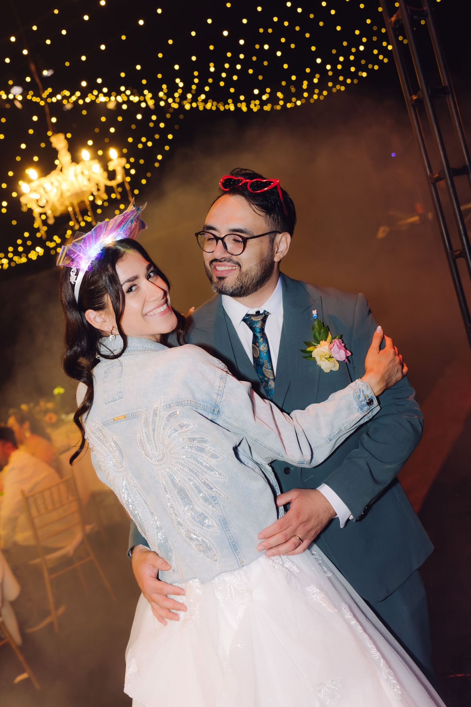 Bride and groom dancing under twinkling chandelier lights at elegant indoor wedding reception.