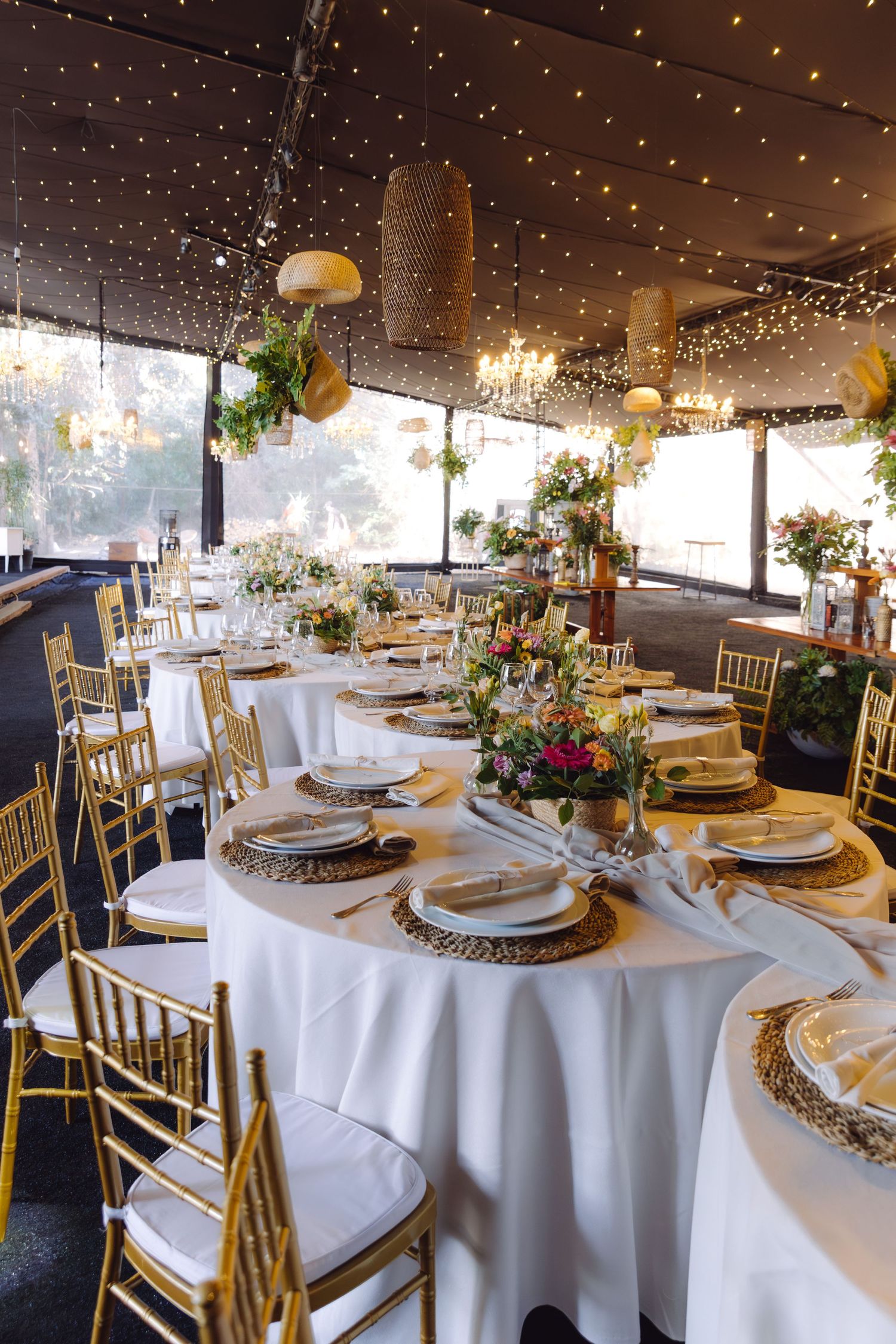 Elegant wedding reception venue with gold chiavari chairs, white tablecloths, and fairy light ceiling decor.