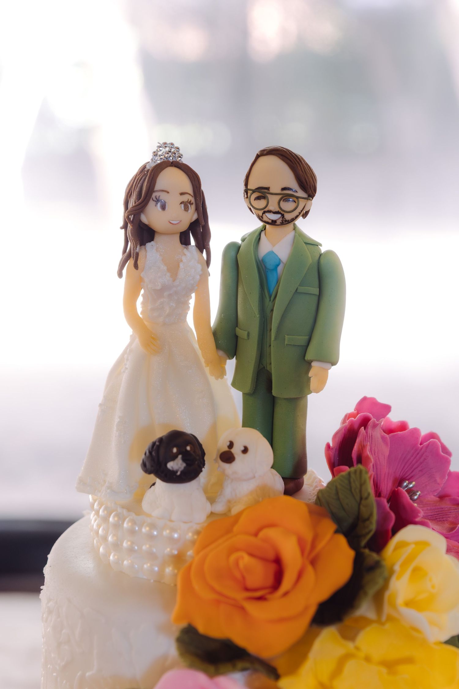Custom wedding cake topper featuring bride in white gown and groom in green suit with two small dogs.