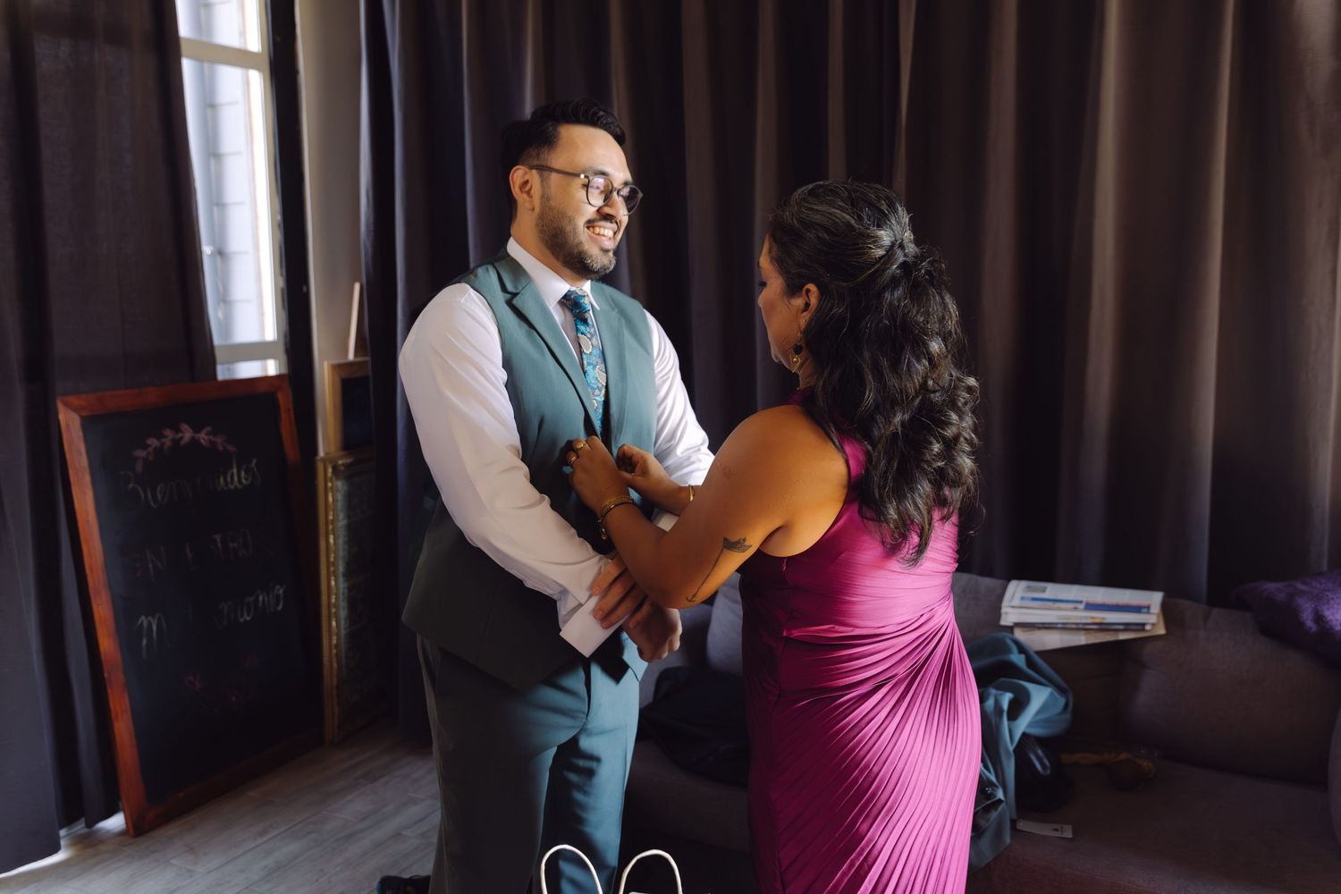 Groom in teal suit sharing a joyful moment with woman in magenta dress before wedding ceremony.