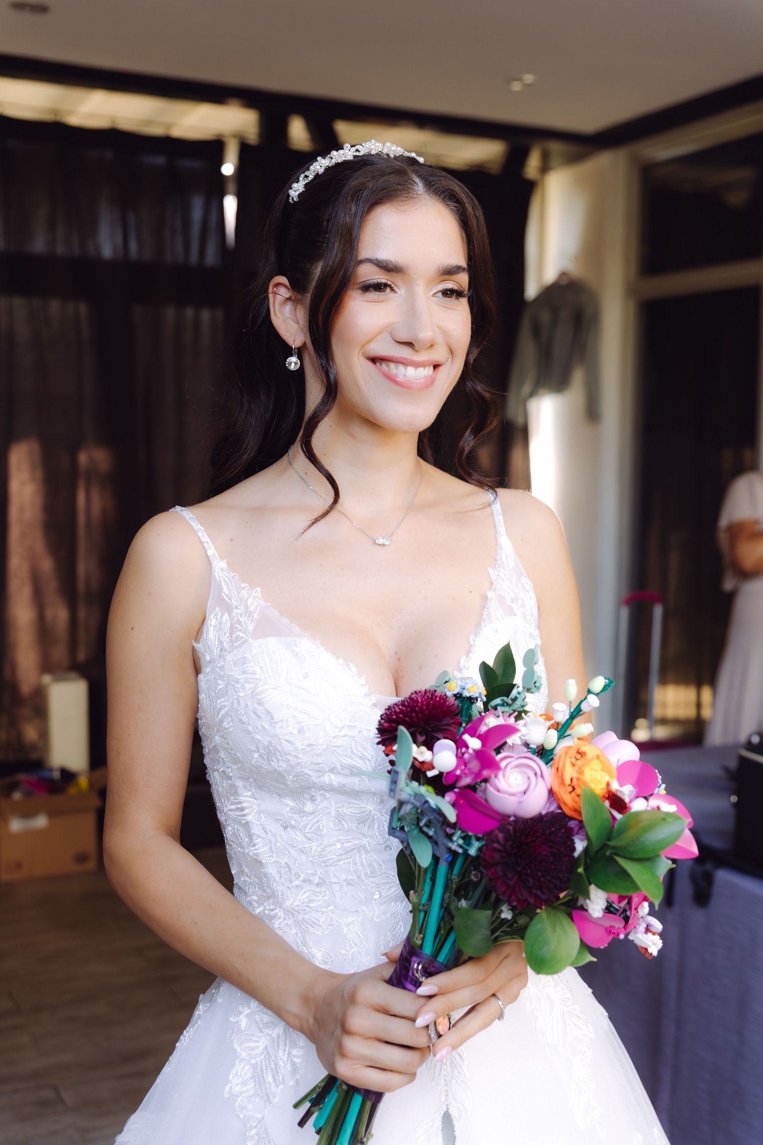 Radiant bride in white lace gown holding colorful bouquet with crystal tiara and drop earrings.