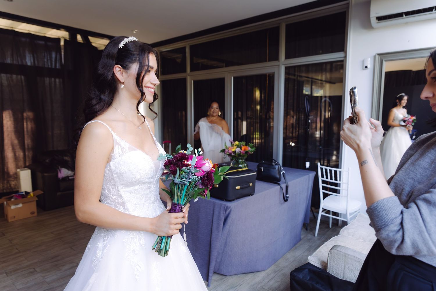 Bride in white wedding dress holding vibrant bouquet while being photographed during bridal preparations.