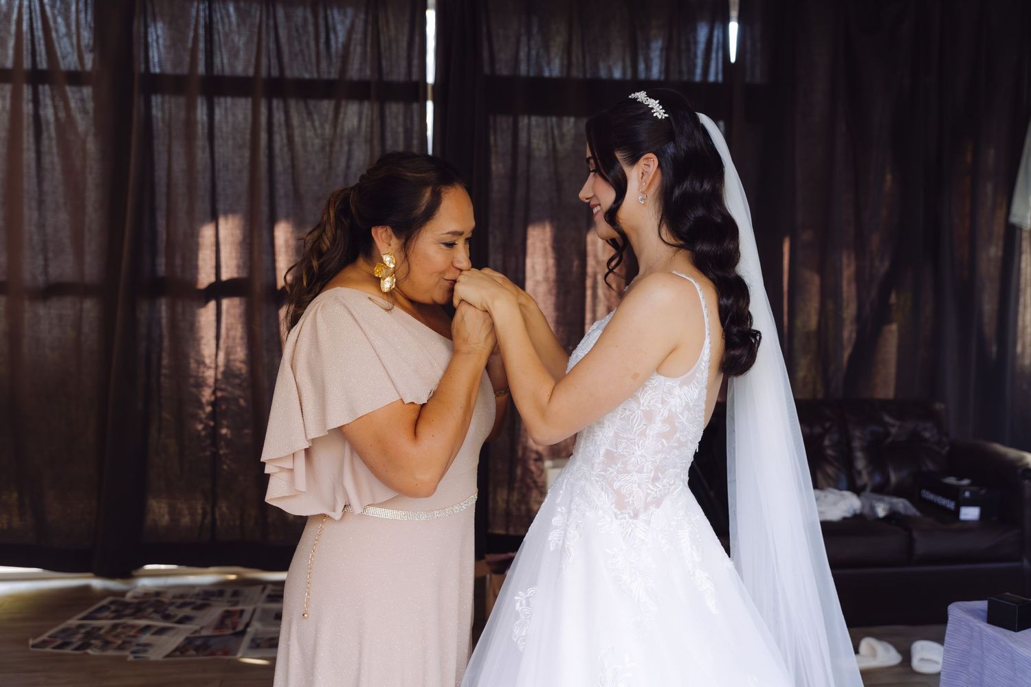 Touching moment as woman in beige dress kisses bride's hand during wedding day preparations.