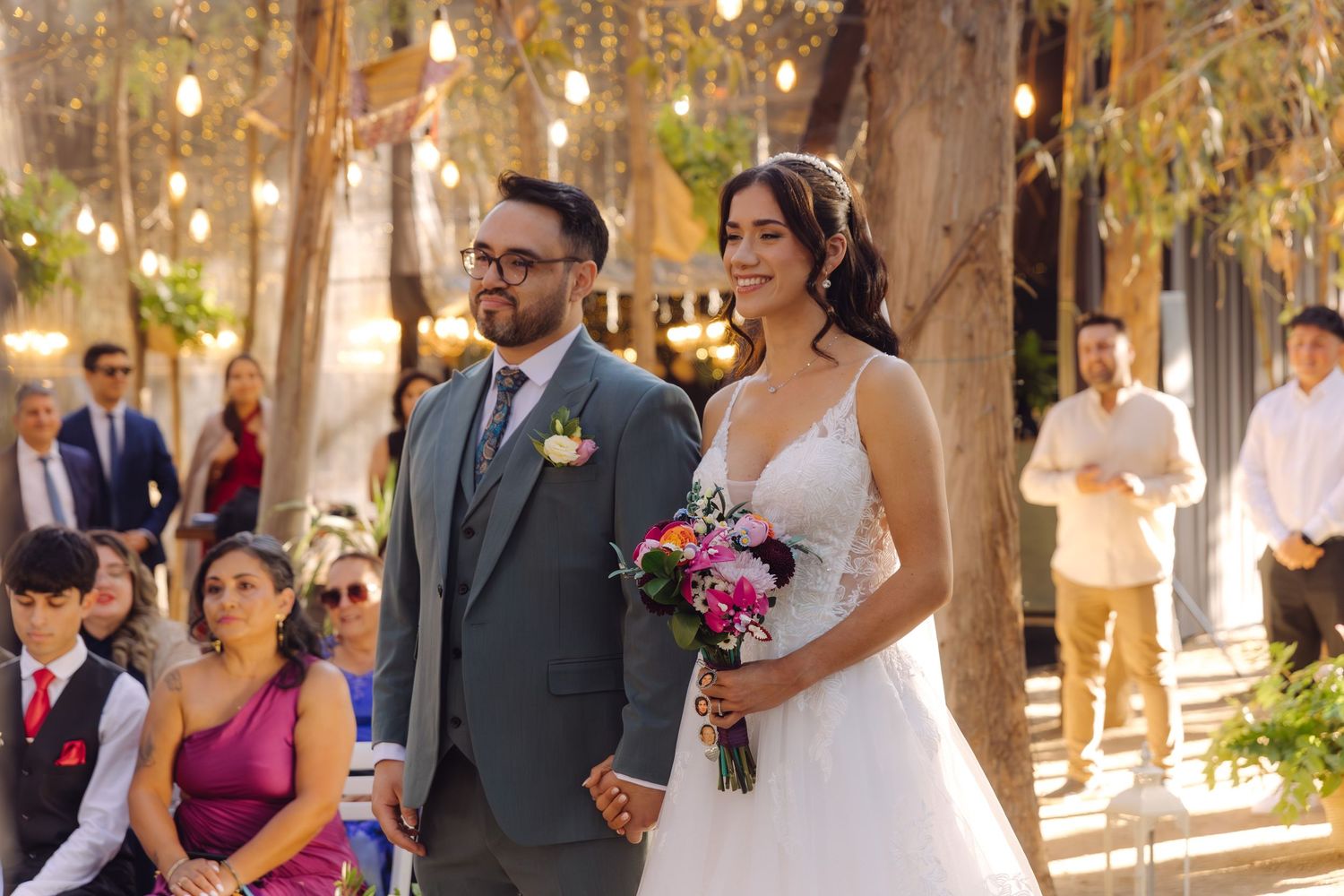 Bride and groom walking hand in hand down the aisle at an outdoor woodland wedding ceremony with guests seated.
