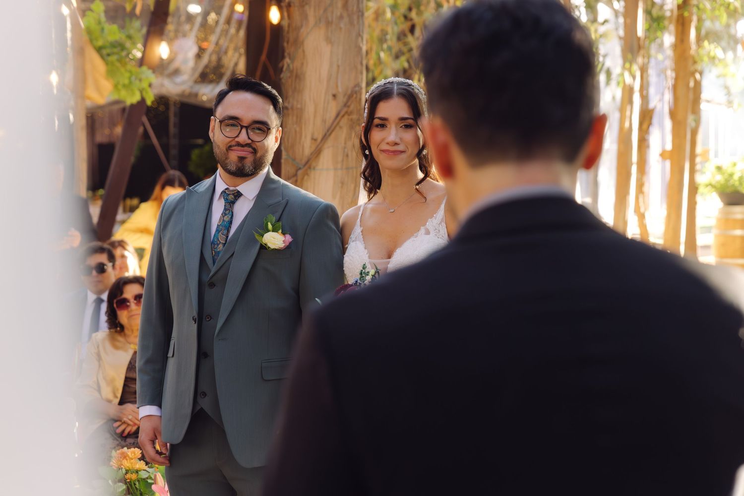 Bride and groom approach altar at outdoor wedding ceremony surrounded by trees and string lights.