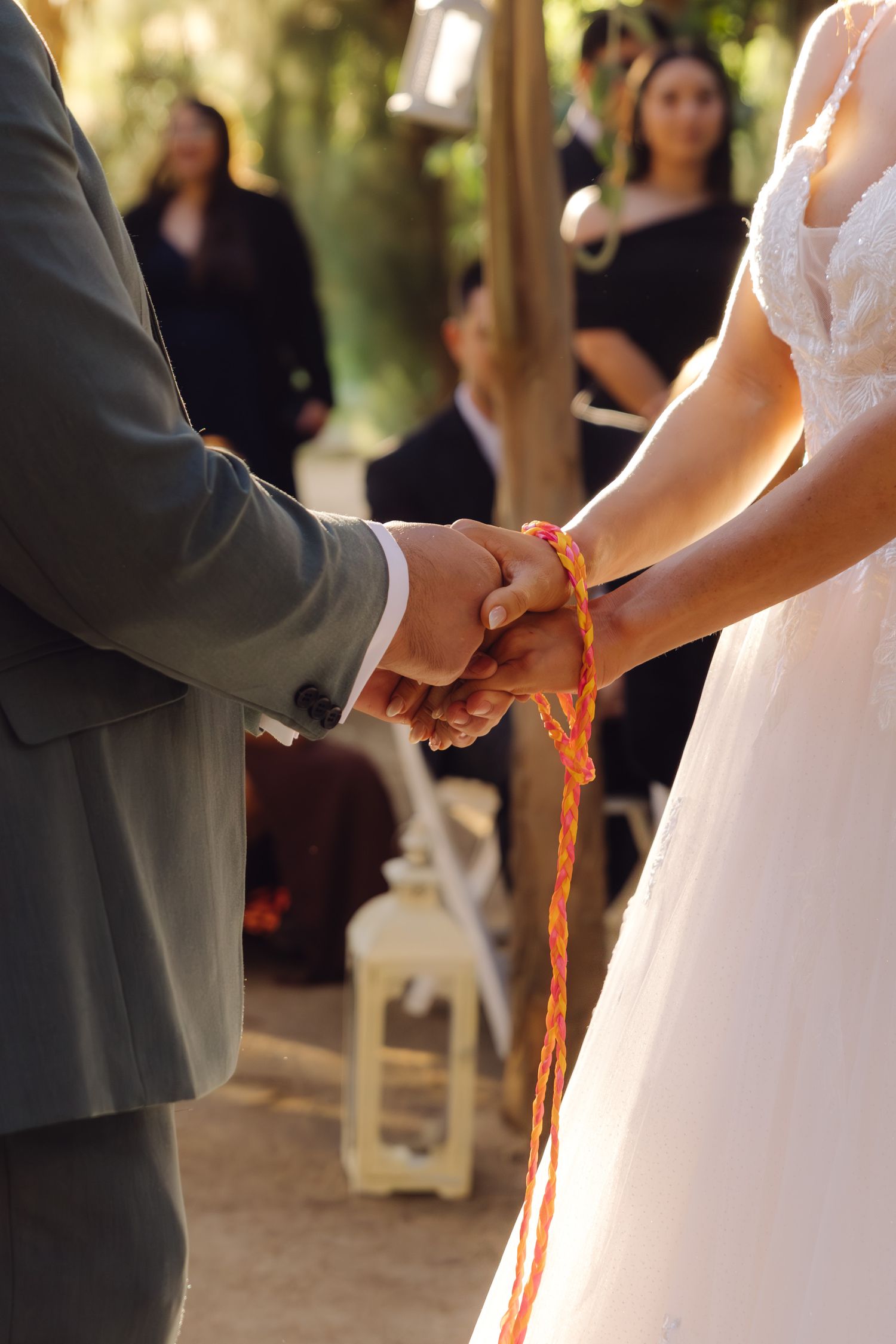 Bride and groom perform a handfasting ceremony with orange ribbon at outdoor woodland wedding.