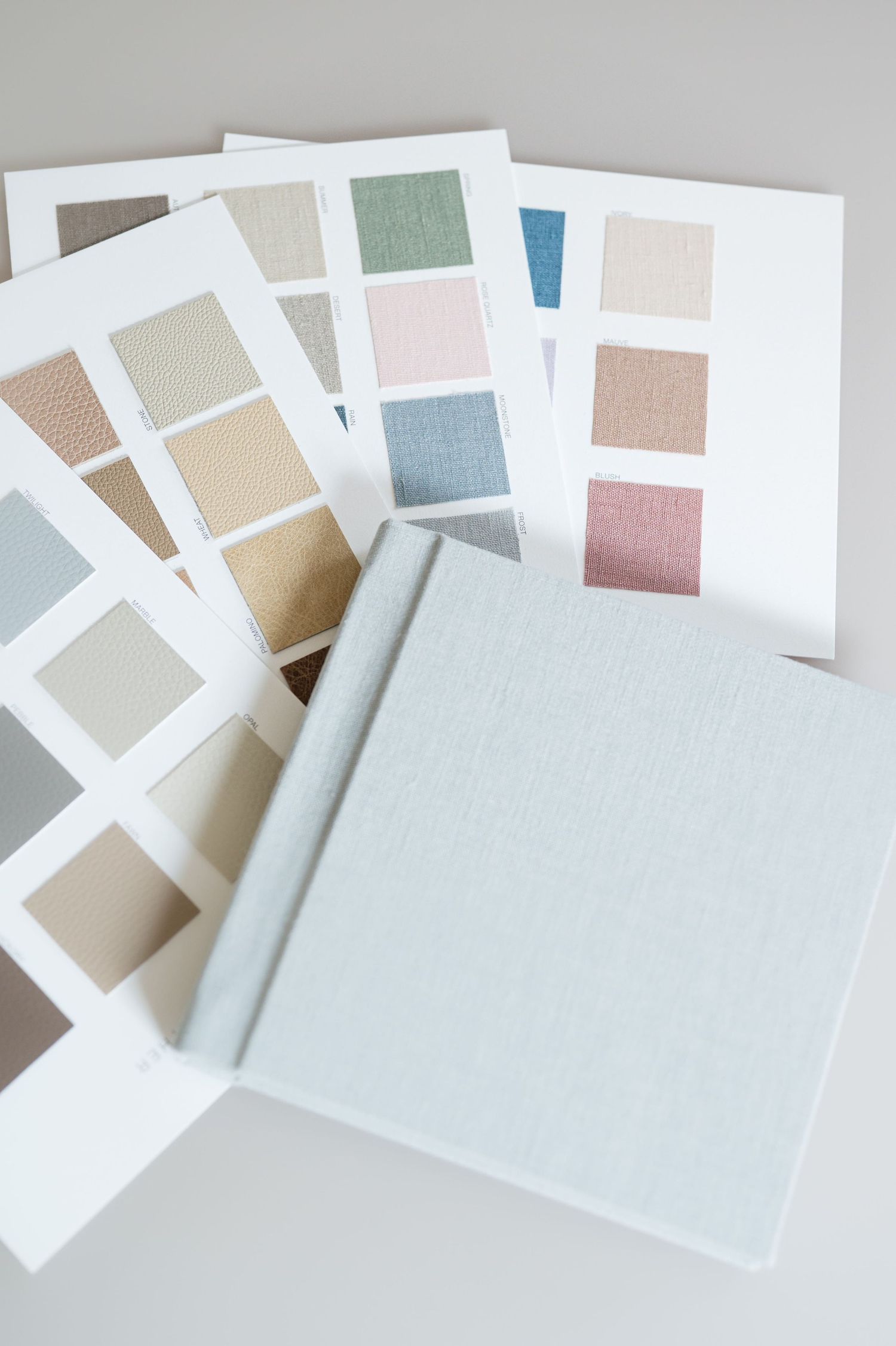 Light blue linen photo album with embossed script text beside fabric color swatches on white background.