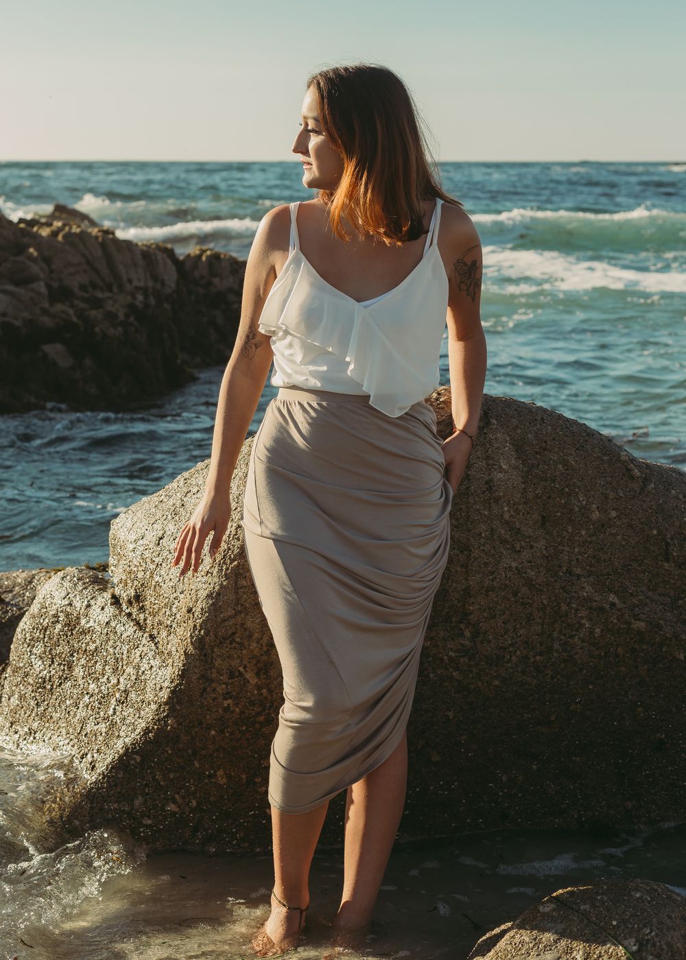 A young woman posing on a rock staring out at the ocean