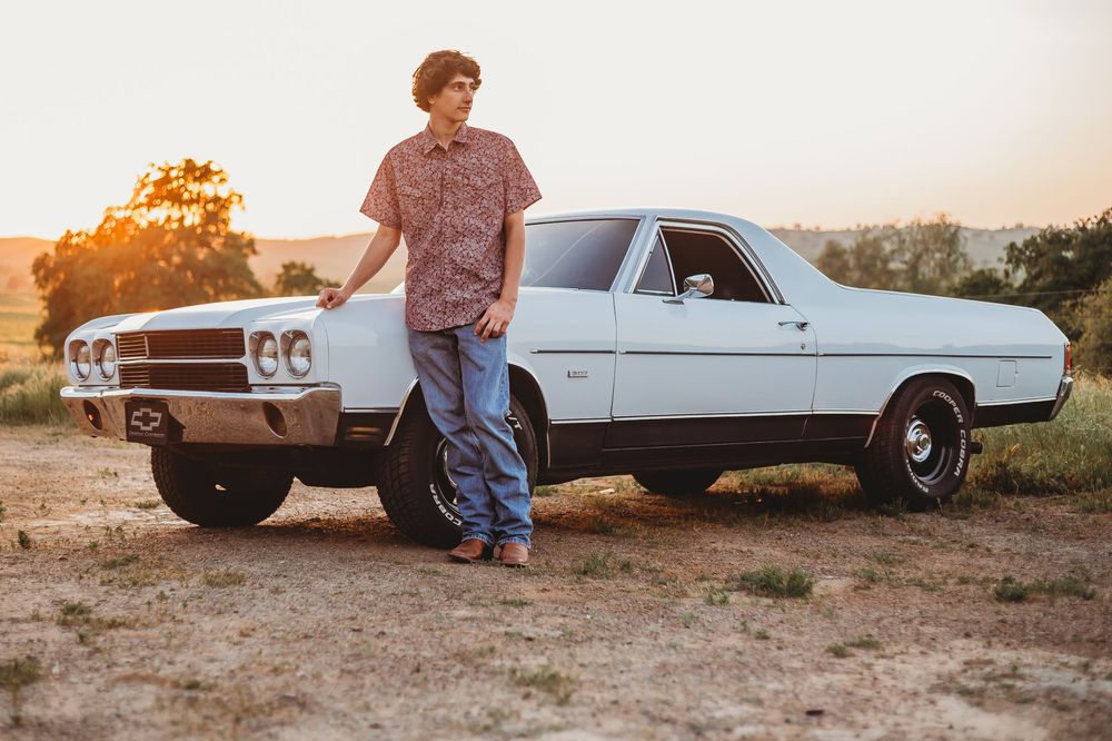 A teenage boy posing in front of his El Camino car