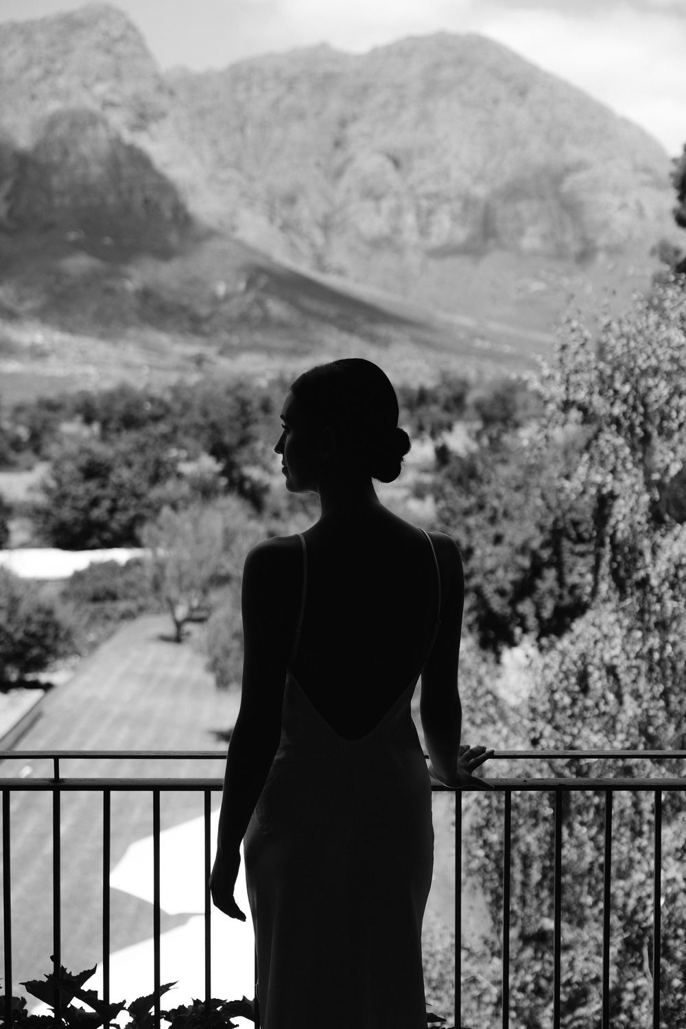 Silhouette of a bride in a backless wedding gown standing on a balcony with mountain views.