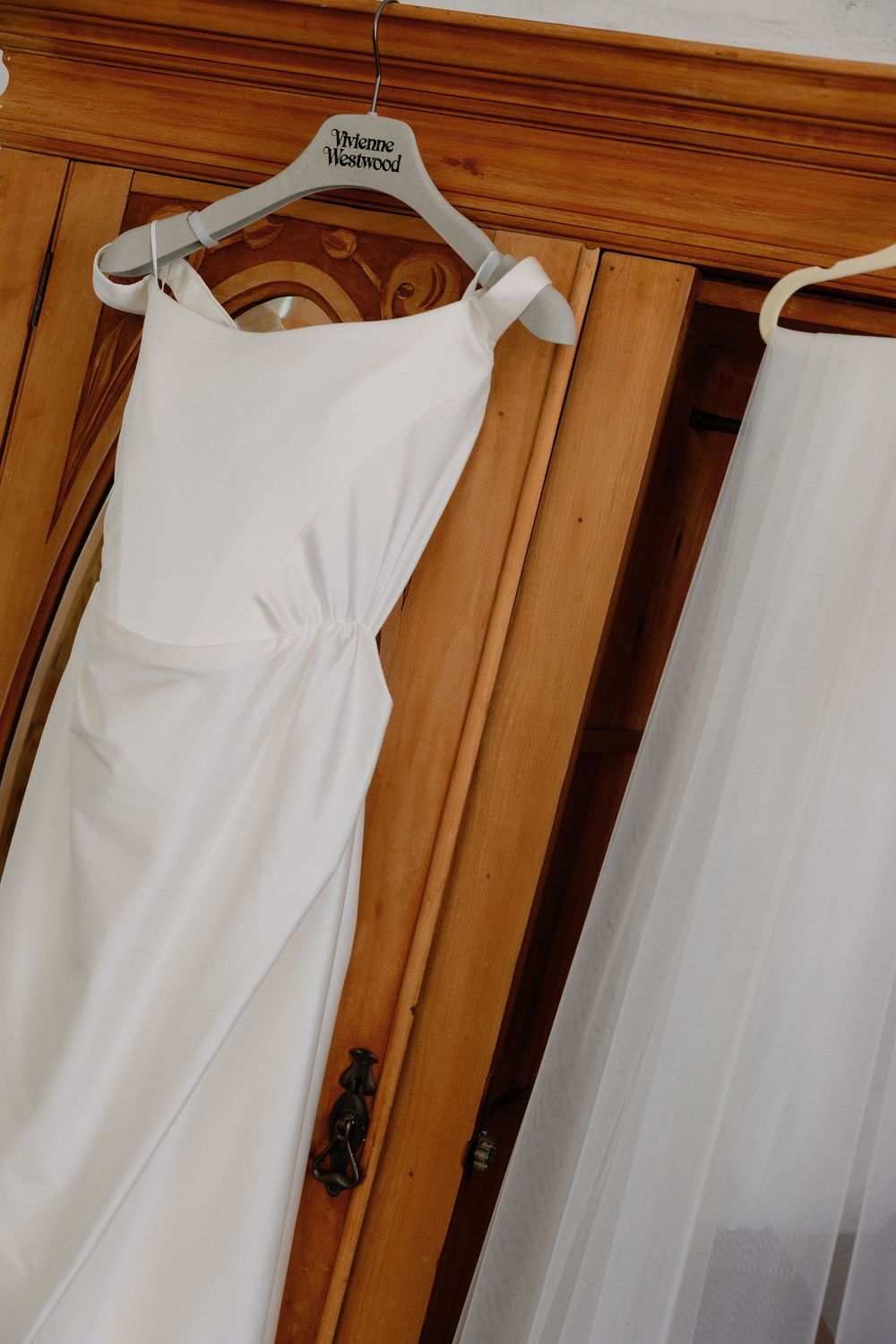 Vivienne Westwood white wedding dress hanging on a wooden wardrobe with a veil.