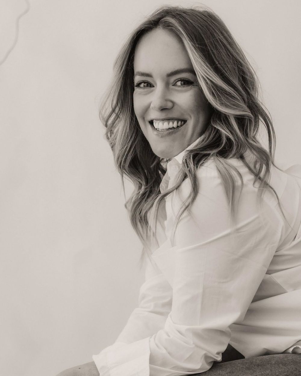 Black and white portrait of a smiling woman with wavy hair wearing a white button-up shirt.