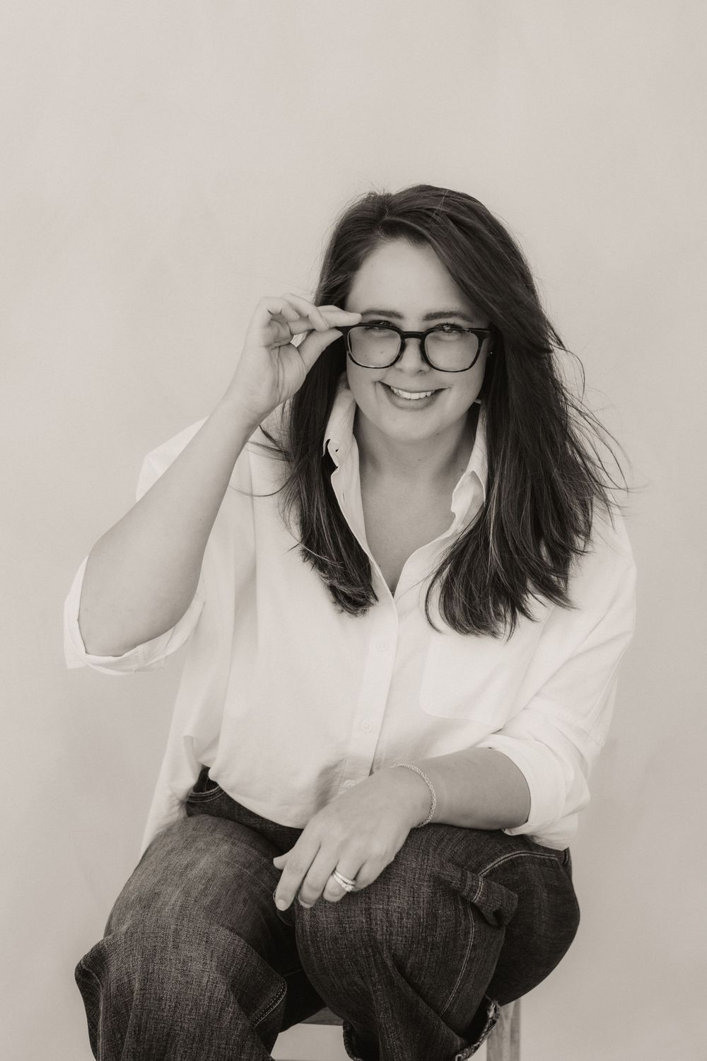 Black and white portrait of a smiling woman with glasses and long dark hair wearing a white shirt.