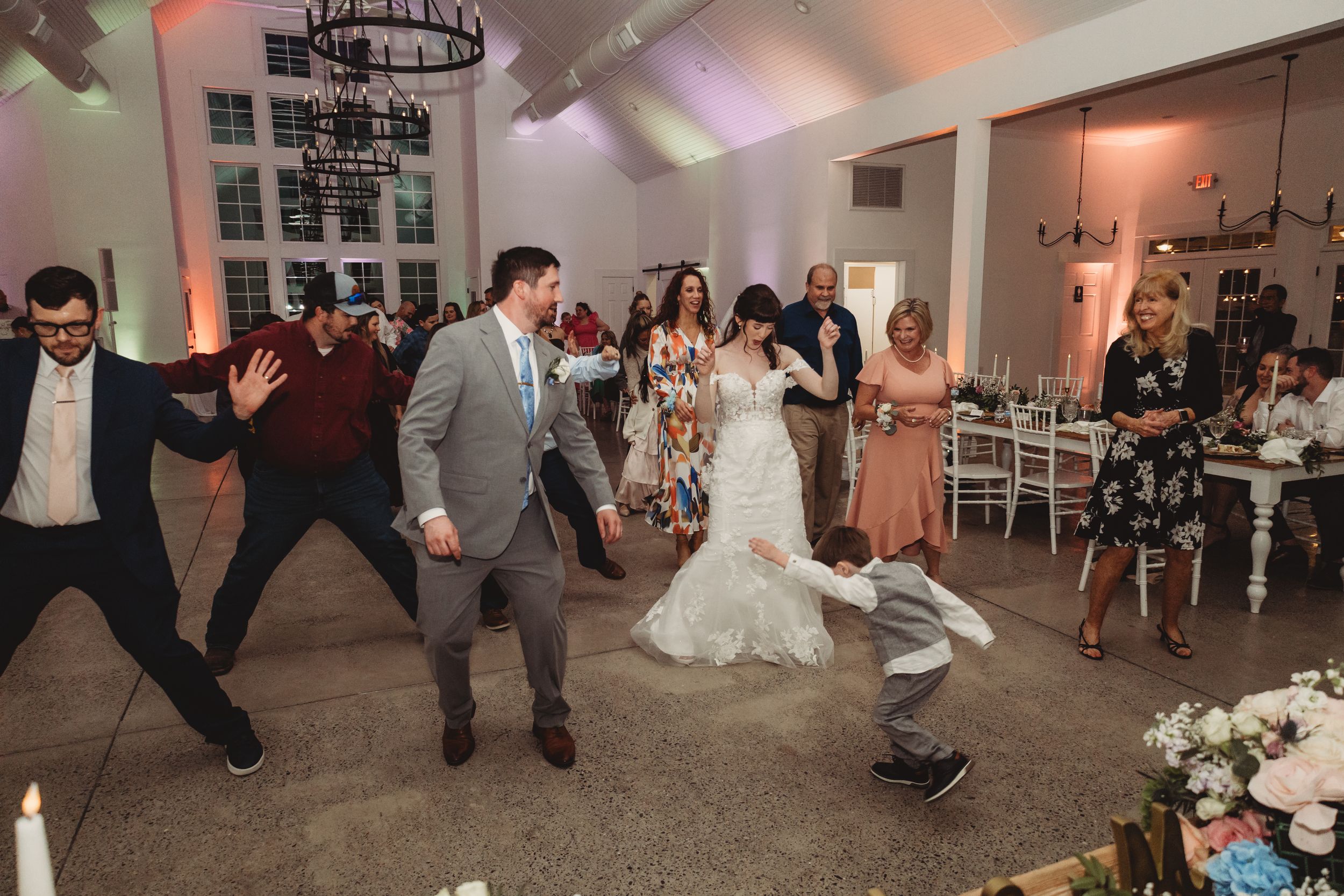 Wedding reception dance floor fun with bride, groom, and guests celebrating joyfully in elegant white venue.