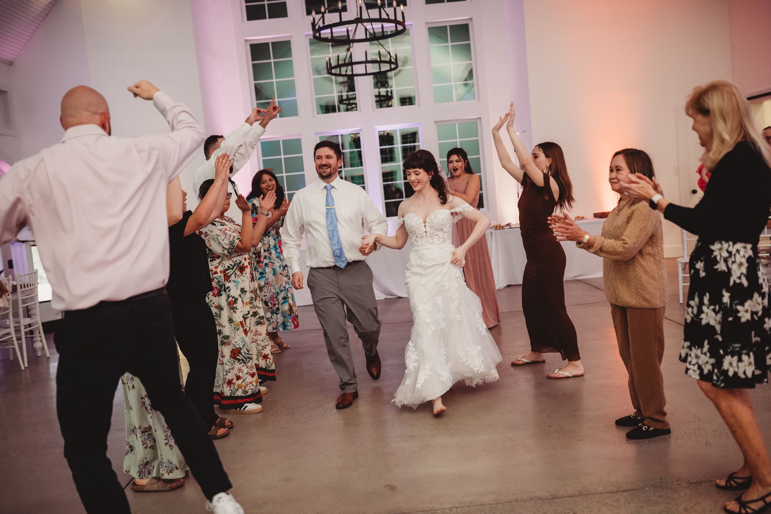 Bride and groom dancing joyfully with wedding guests in elegant white reception venue.