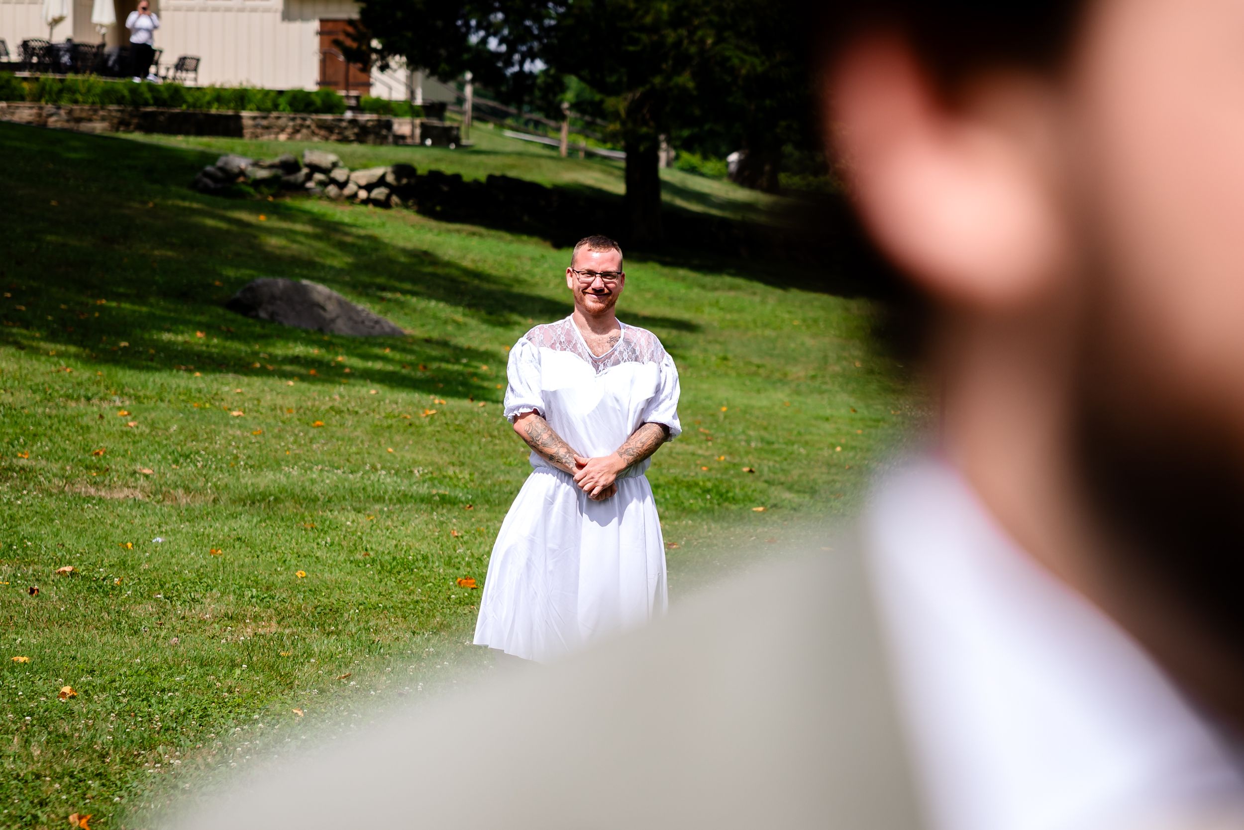 Bride in white gown stands smiling on green lawn during outdoor wedding first look.
