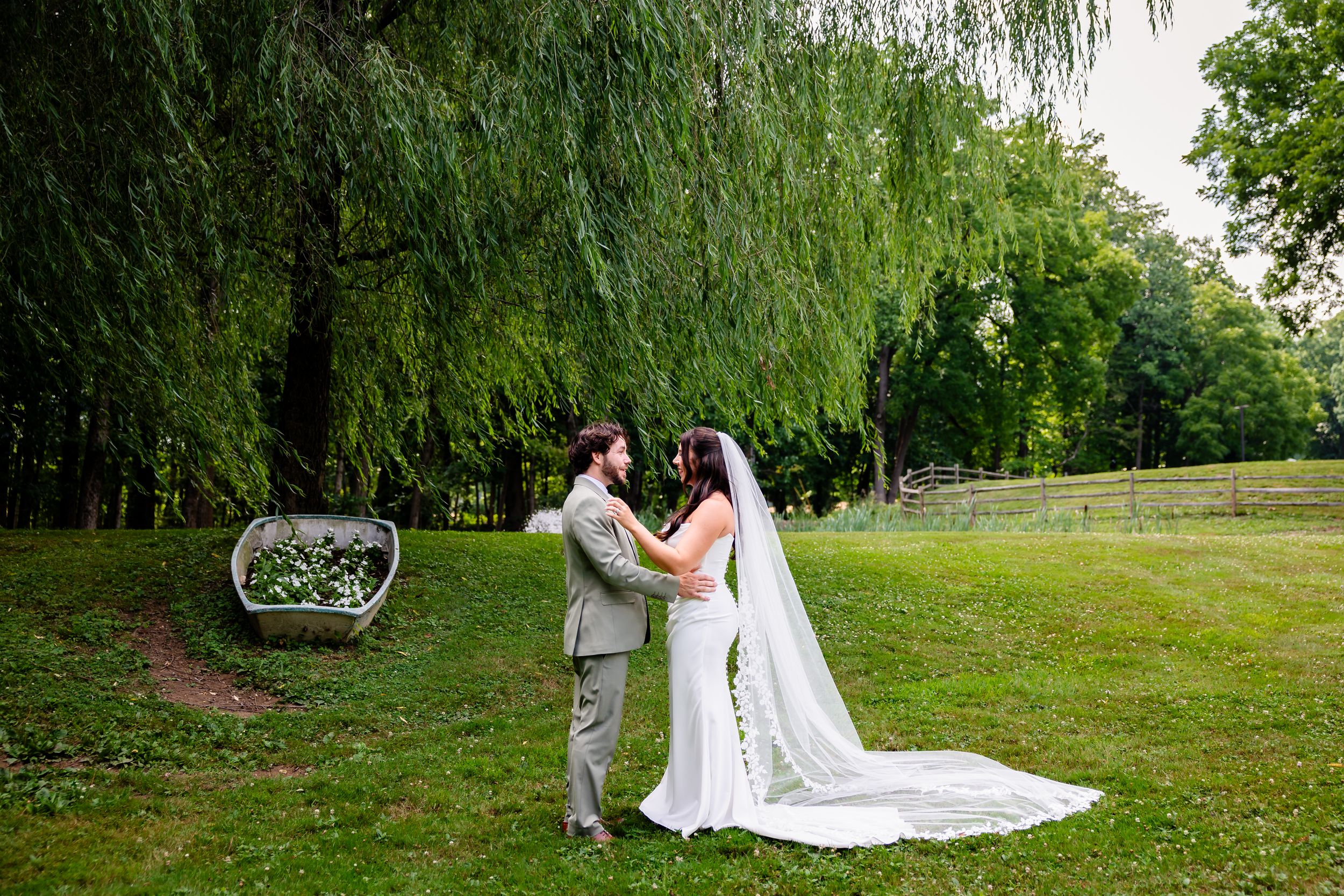 Bride and groom share romantic moment under weeping willow tree at outdoor garden wedding.