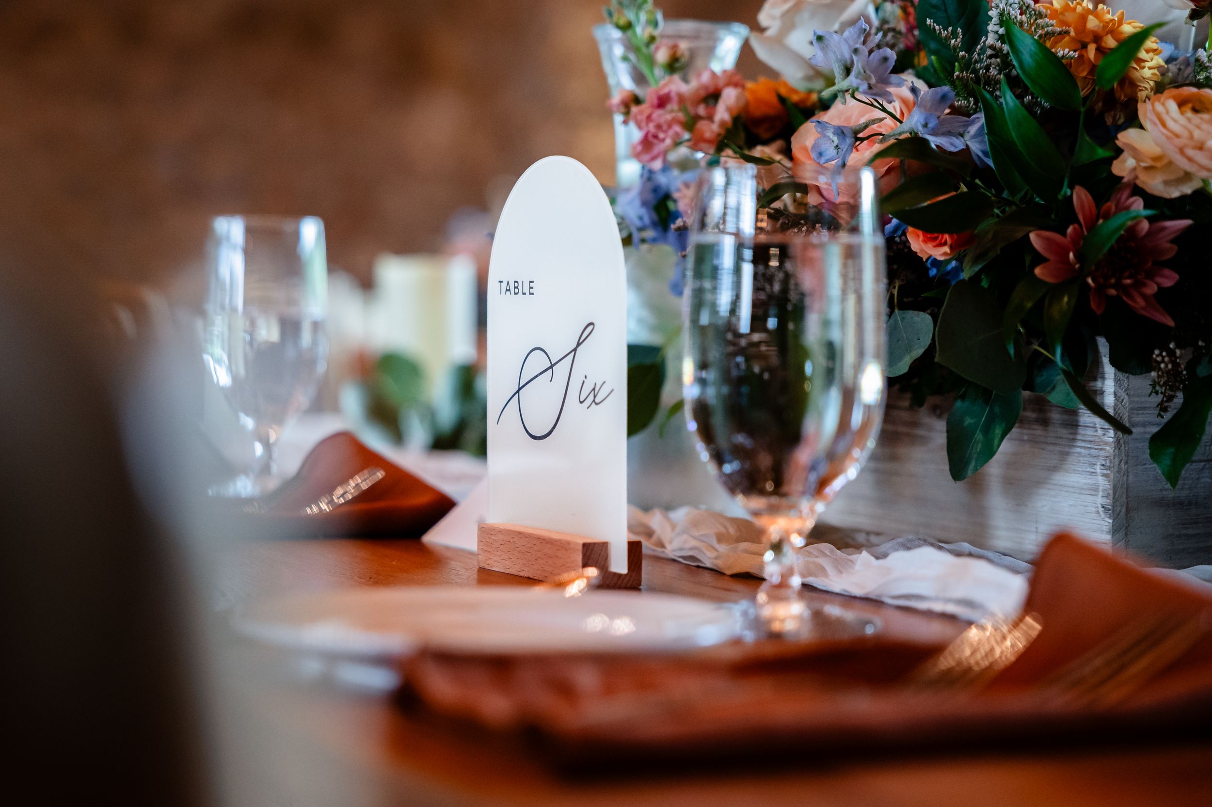 Elegant wedding table setting with arch-shaped Table Six sign, crystal glasses, and colorful floral centerpiece.