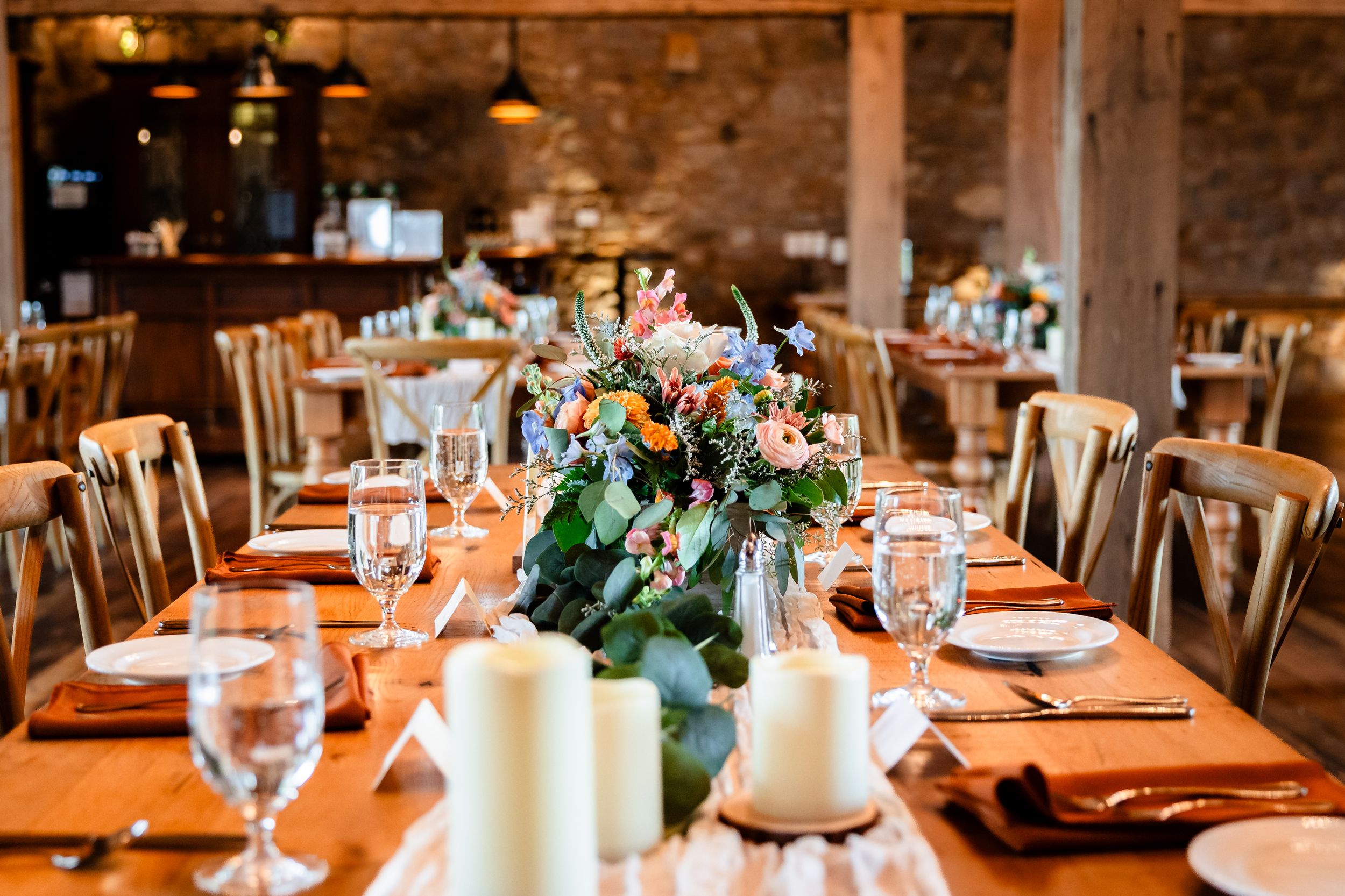 Elegant rustic wedding reception table with floral centerpiece, candles, and place settings in a barn venue.