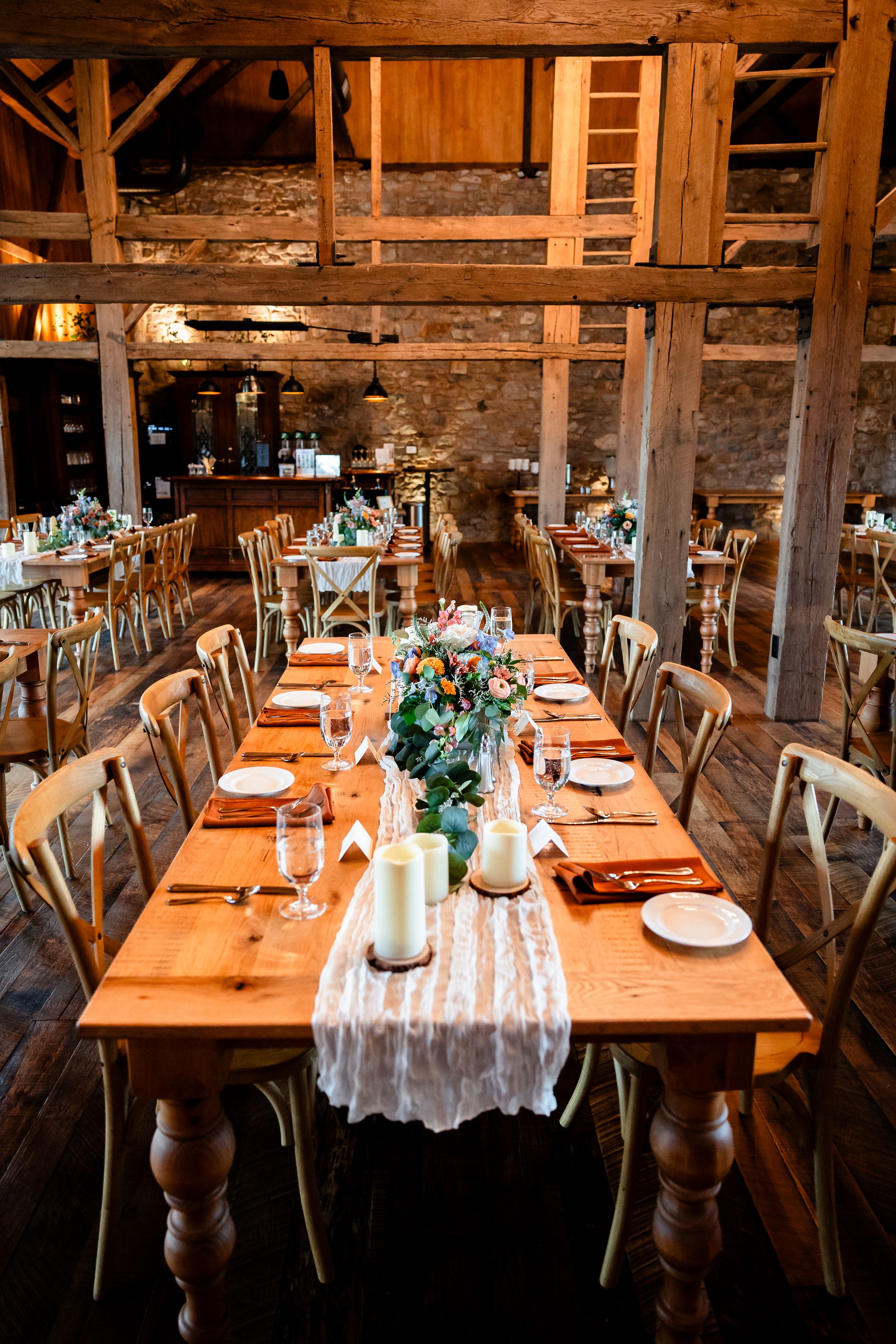 Rustic barn wedding reception with long wooden farm tables, candles, and floral centerpieces.