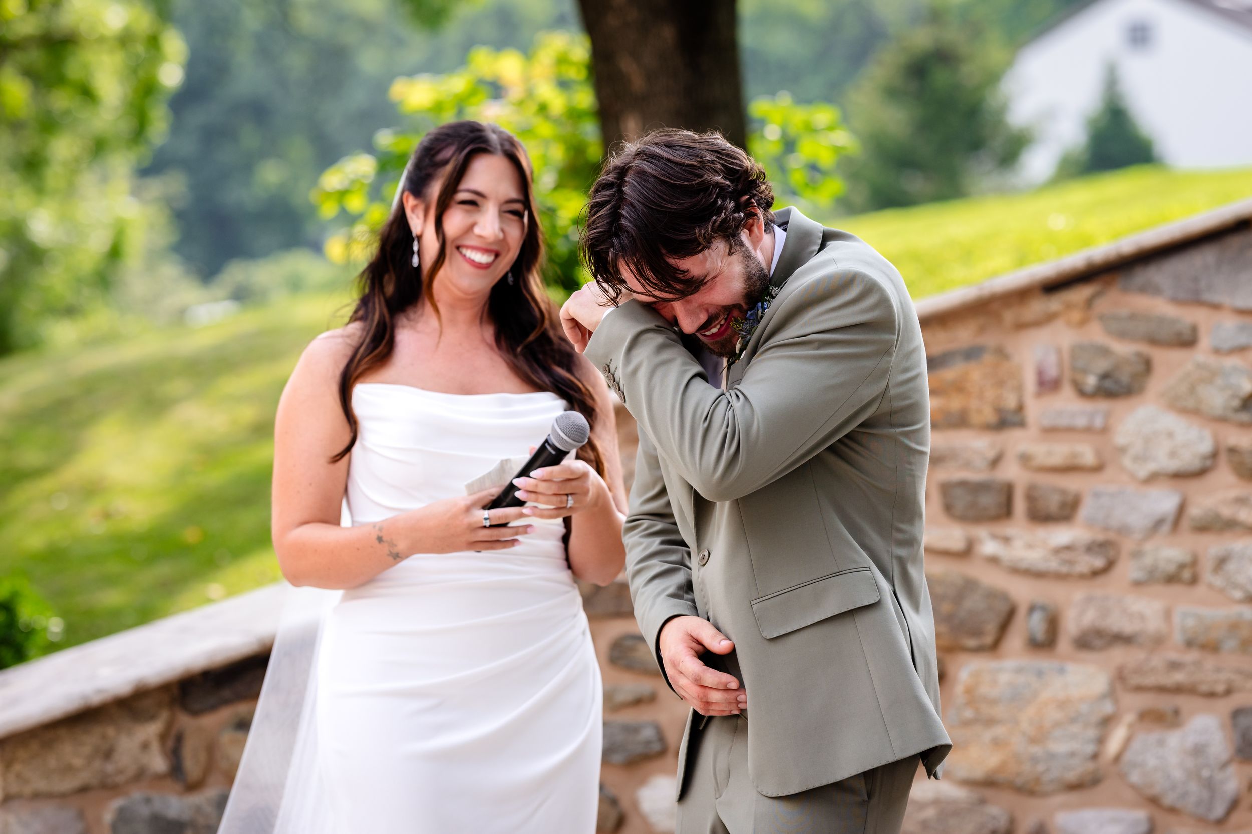 Emotional groom wipes tears while bride smiles during heartfelt first look at stone wall venue.