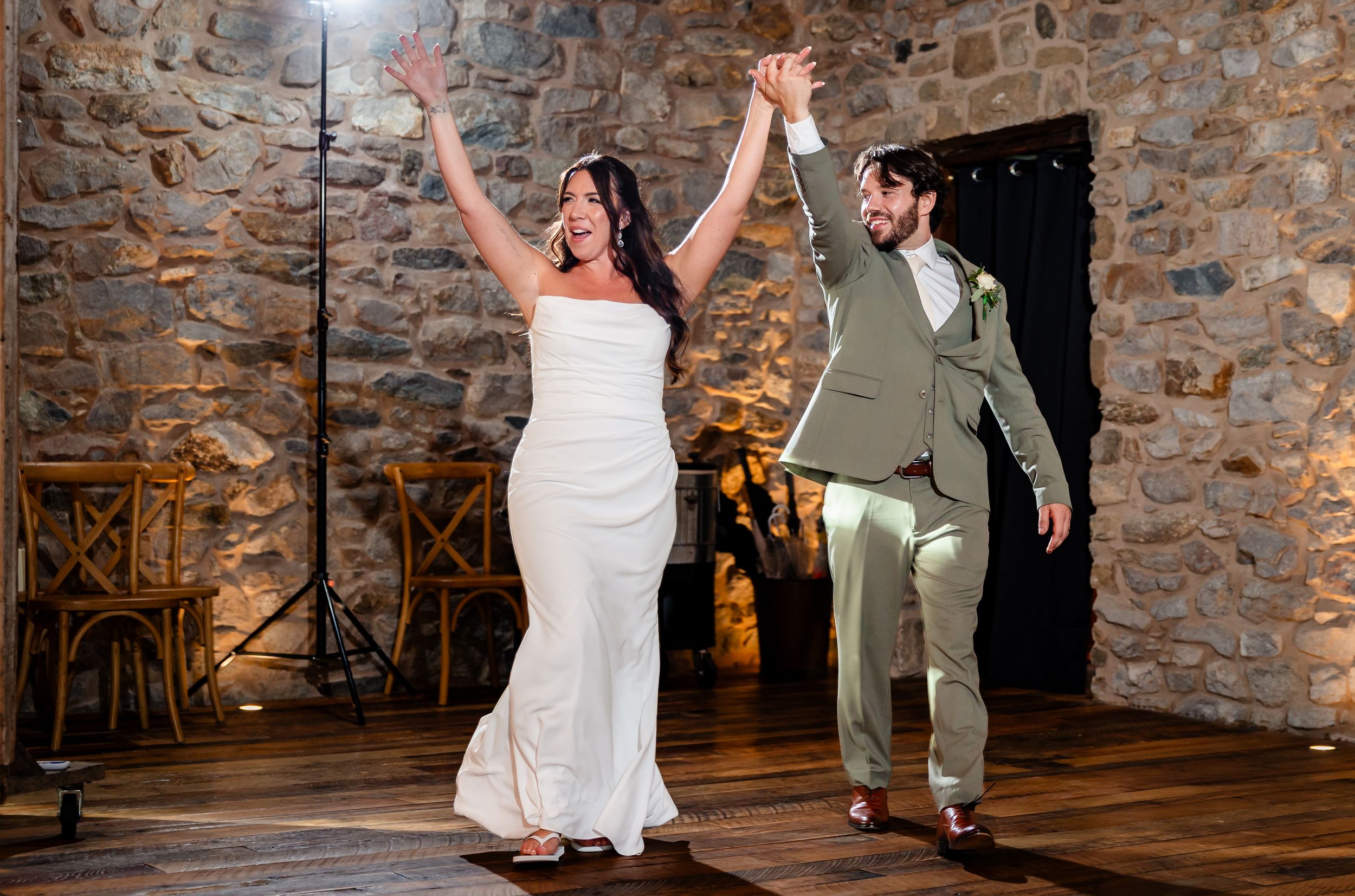Bride and groom celebrate joyfully on dance floor in rustic stone venue during wedding reception.