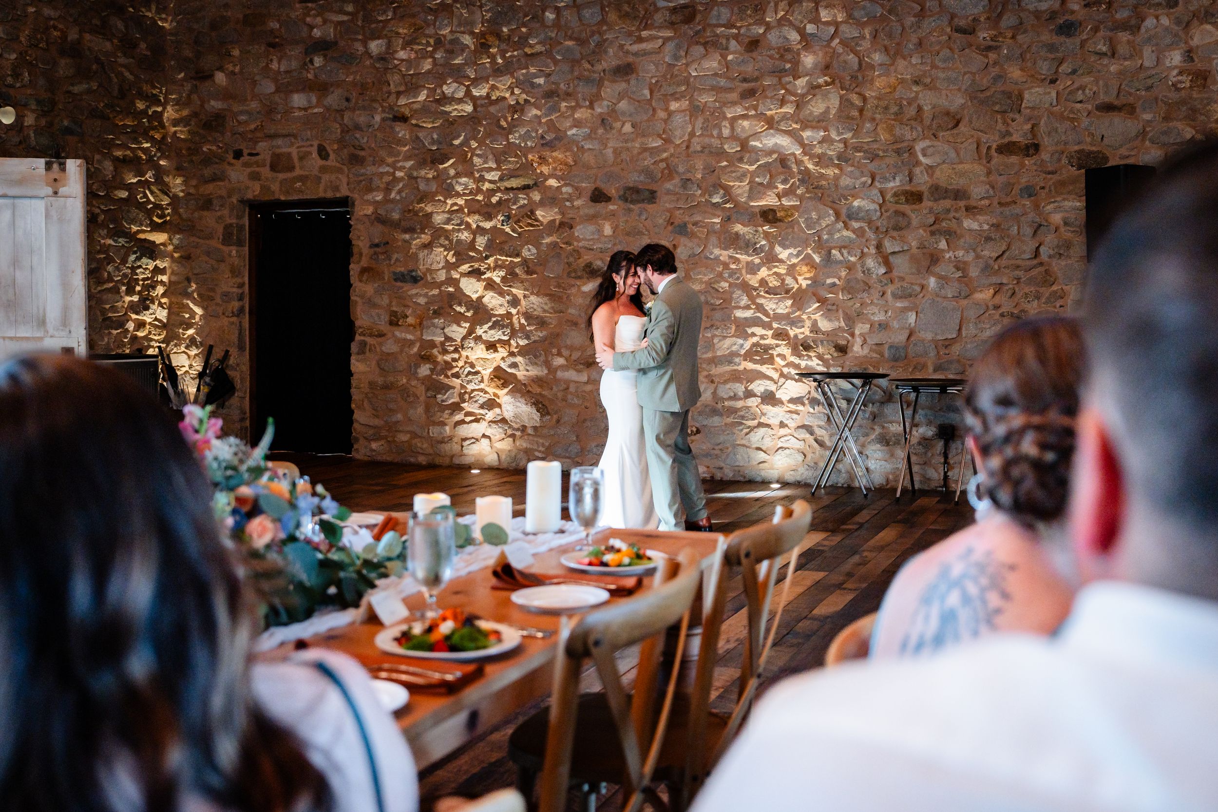 Couple shares first dance in rustic stone barn wedding venue while guests watch from decorated reception tables.
