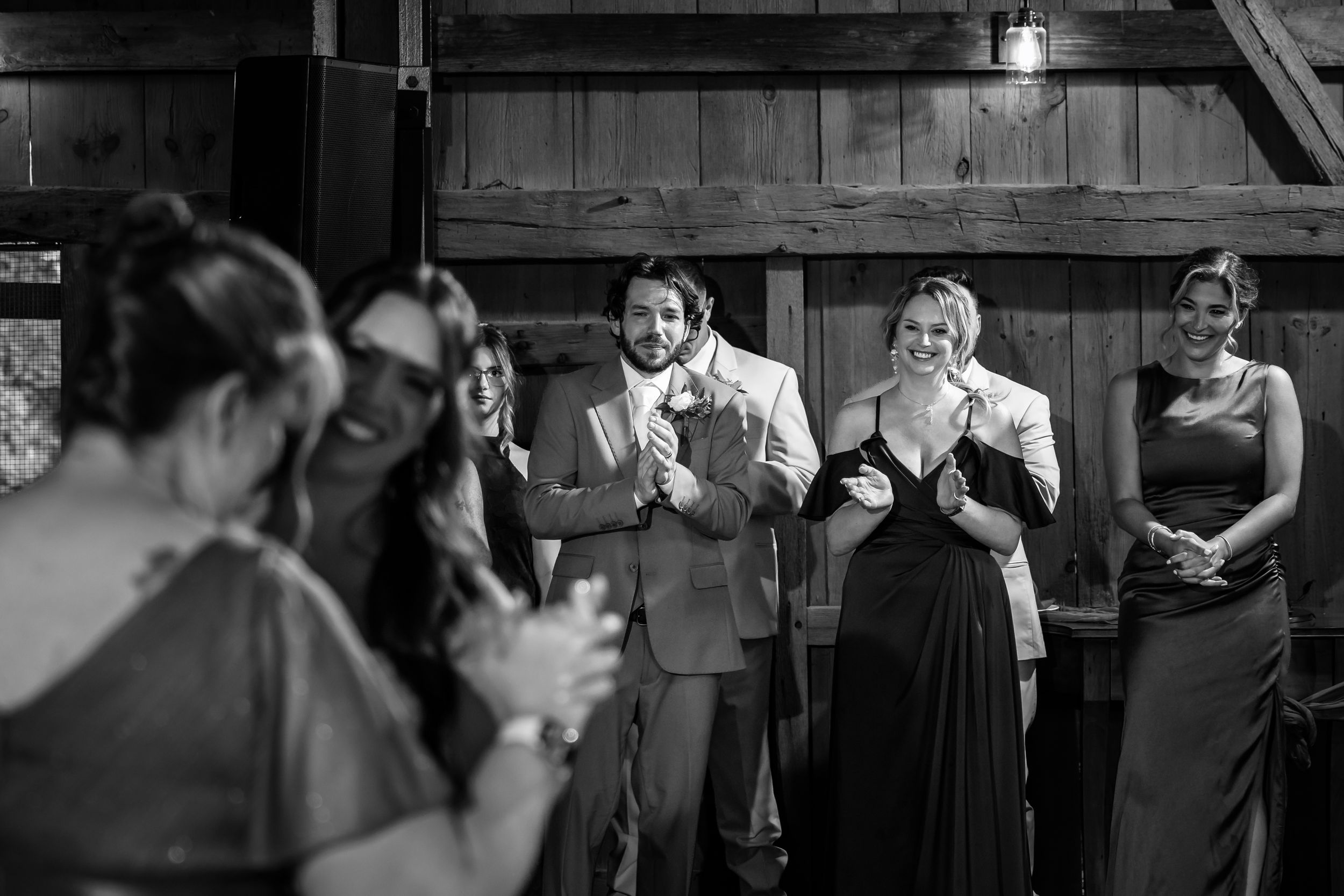 Guests smile and applaud during a wedding reception inside a rustic barn venue.