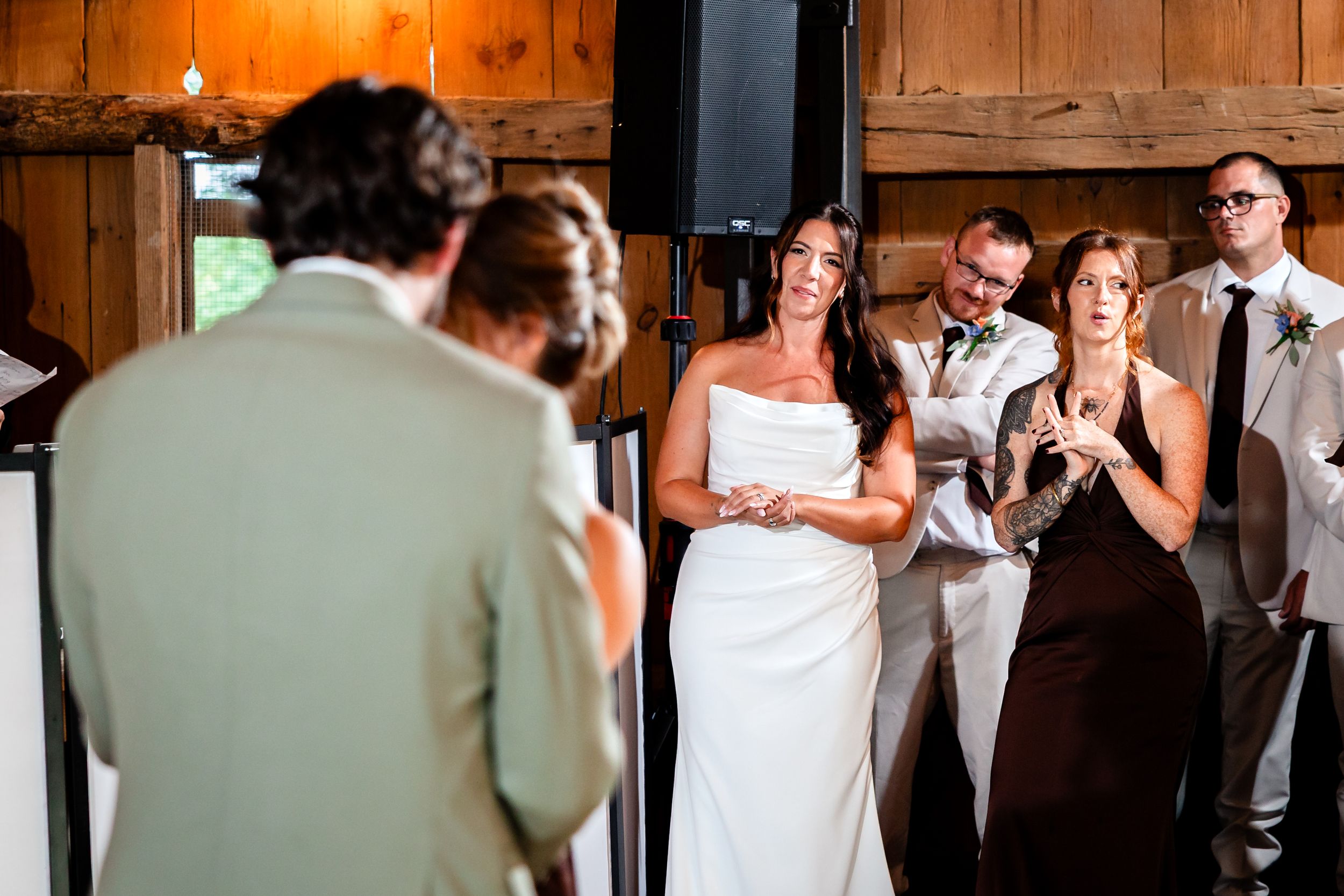 Bride in white strapless gown listens emotionally to groom's vows during indoor barn wedding ceremony.