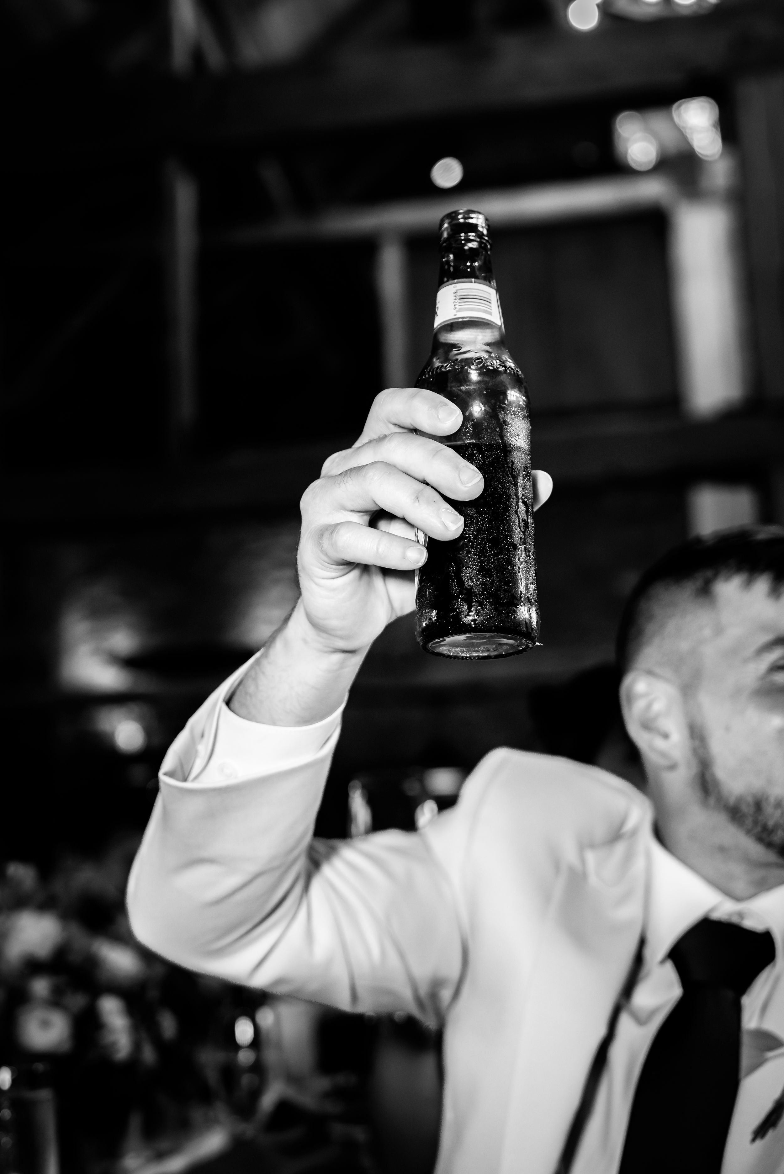 Man in white suit raising a beer bottle in a black and white photo at a bar or event.