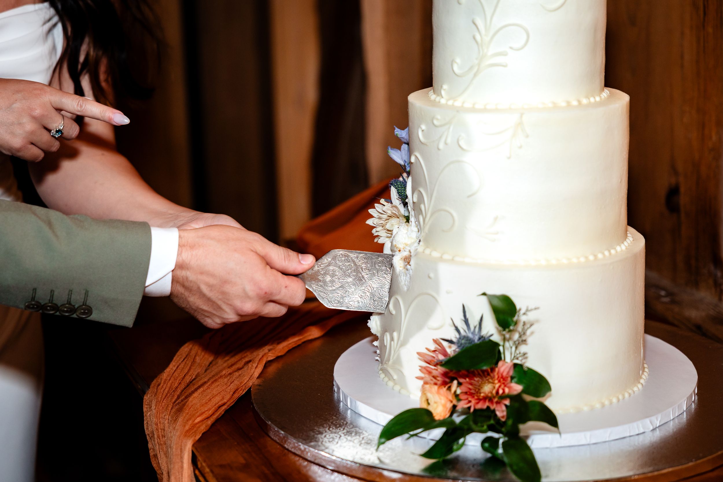 Couple cuts elegant three-tier white wedding cake decorated with flowers.