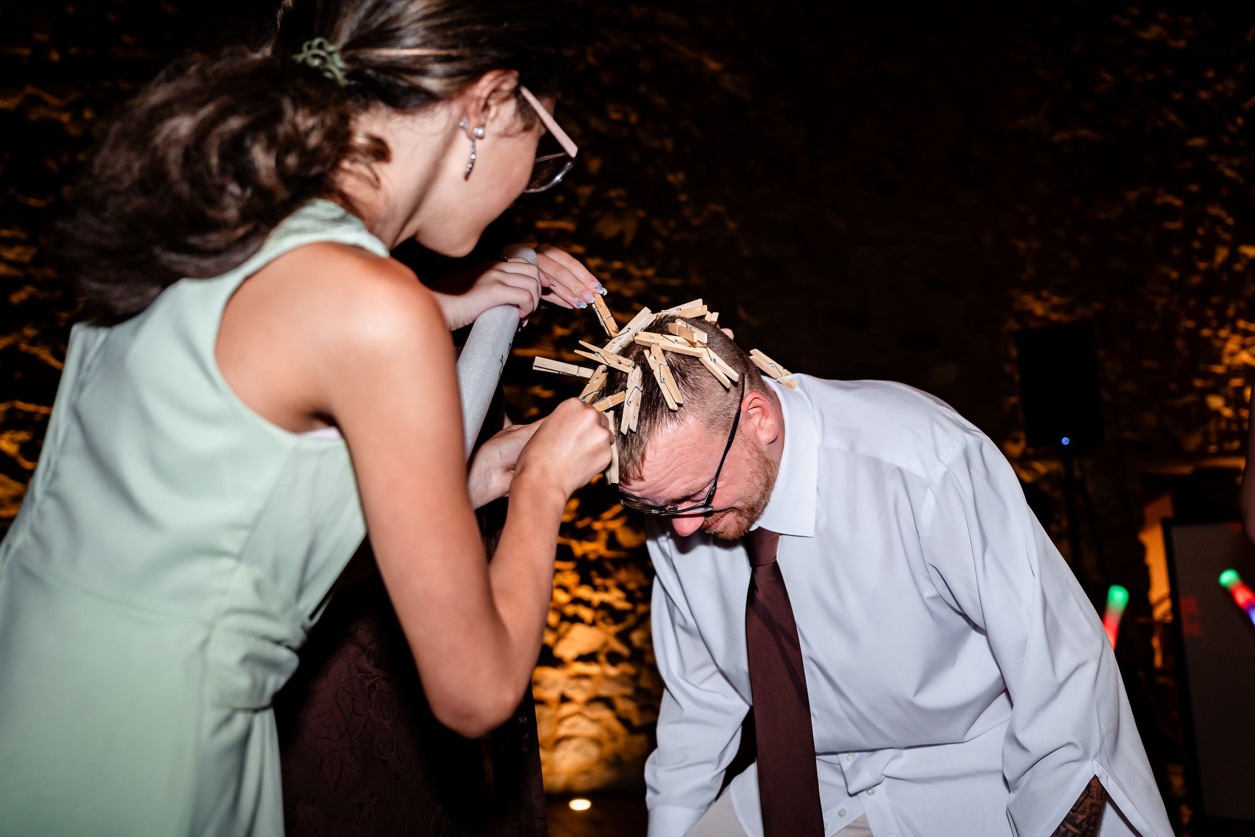 Wedding guest placing floral crown on man's head during outdoor evening reception celebration.