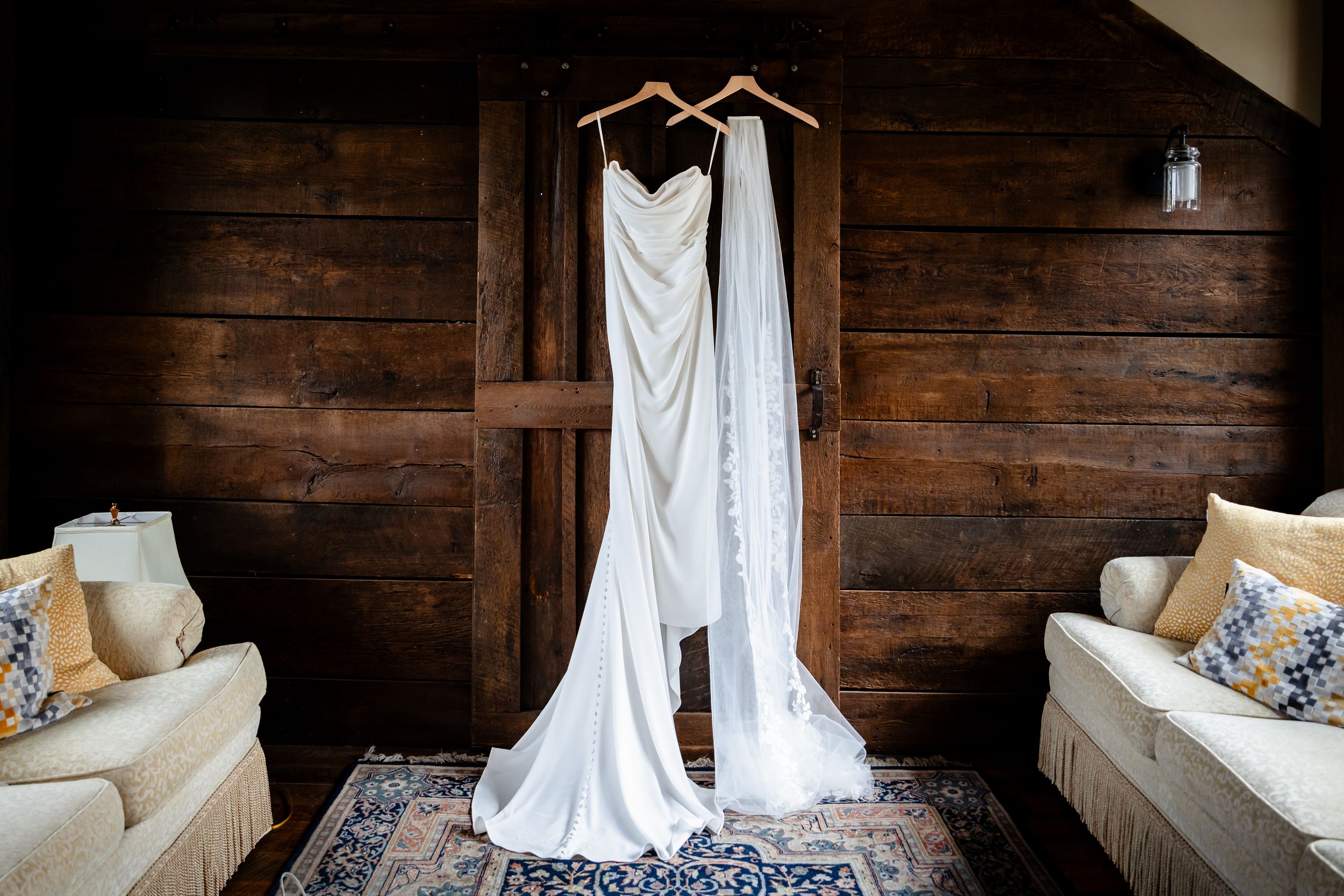 White wedding gown and veil hanging on wooden hangers against rustic wood wall in elegant bridal suite.