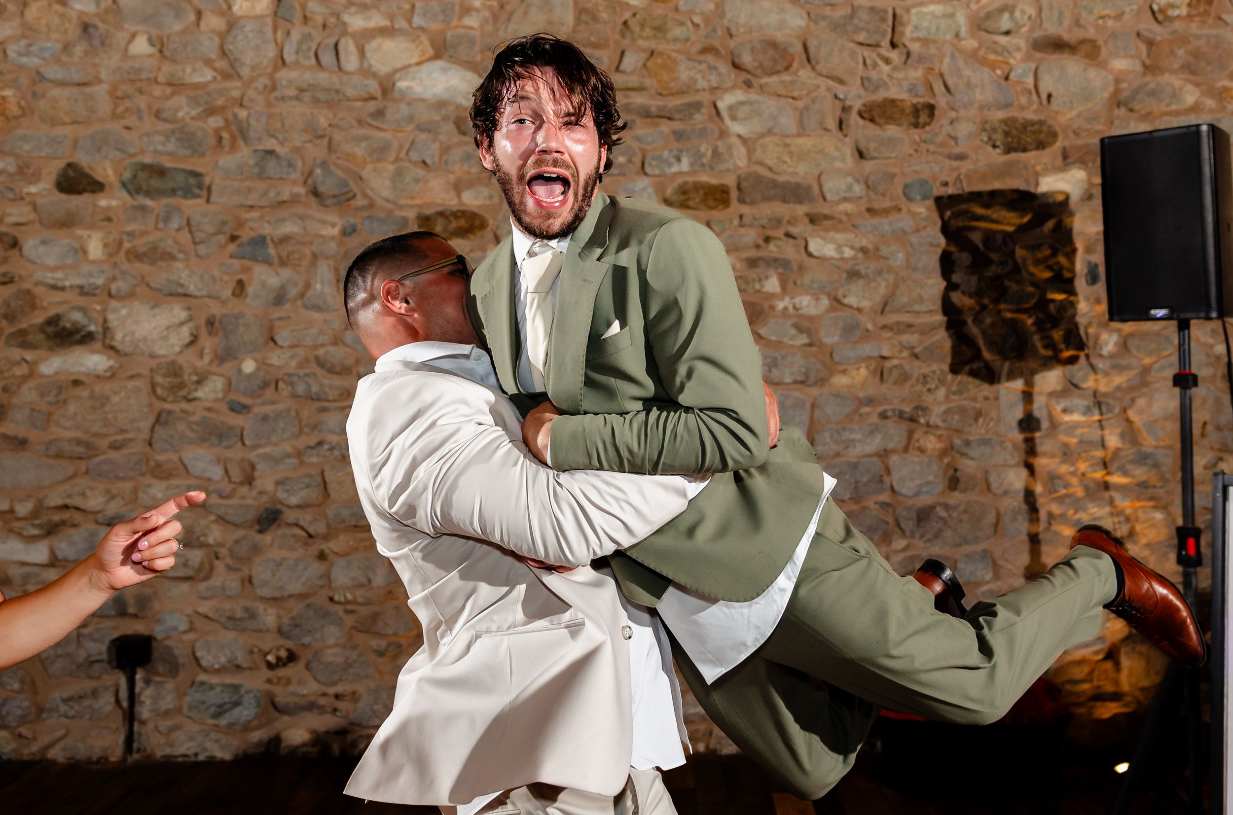 Groomsman joyfully lifts another guest during lively wedding reception dancing.