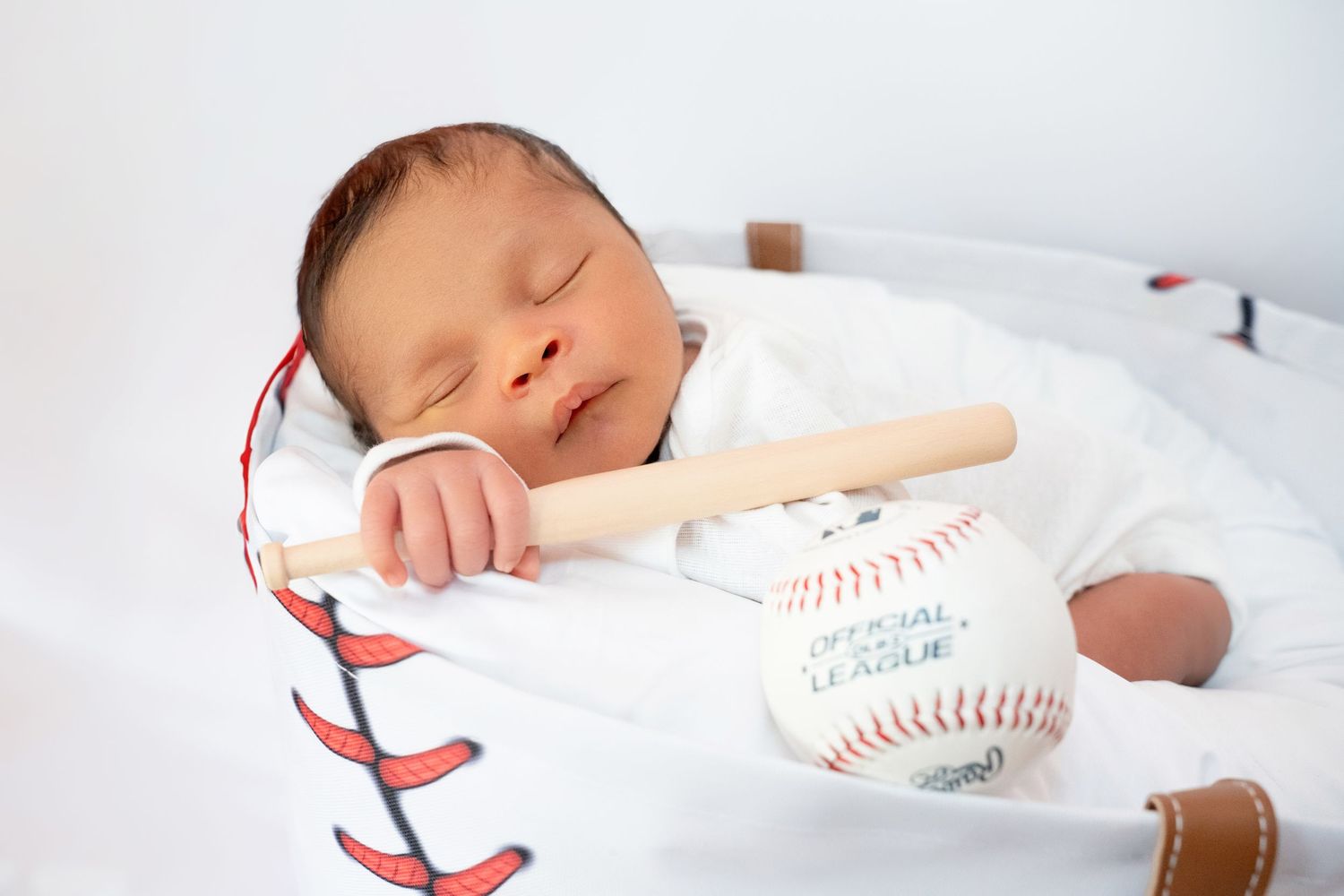 Sleeping newborn baby in baseball glove prop holding a tiny bat and official league baseball.
